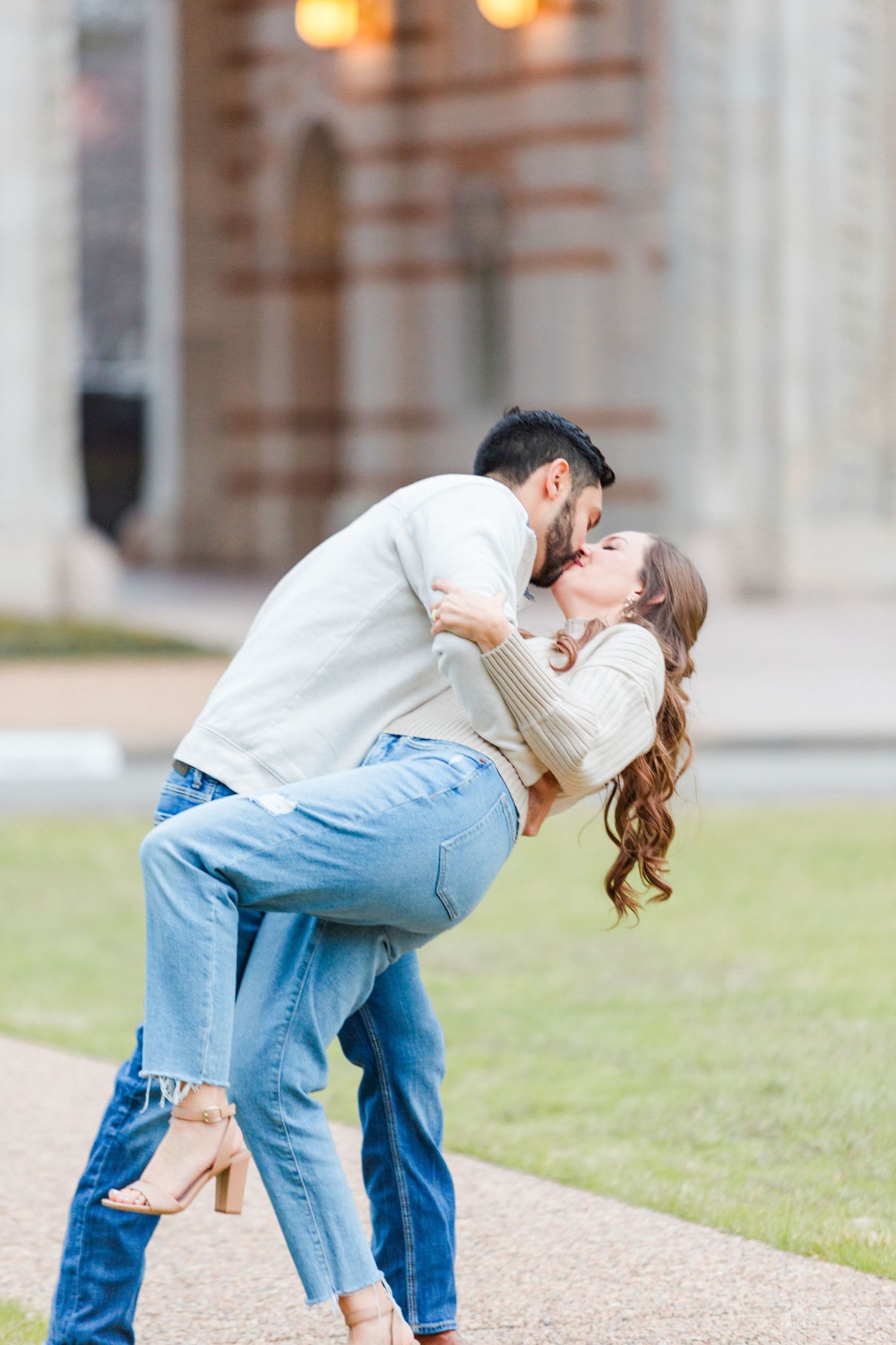 Couple sharing romantic dip kiss pose on pathway near ornate architecture.