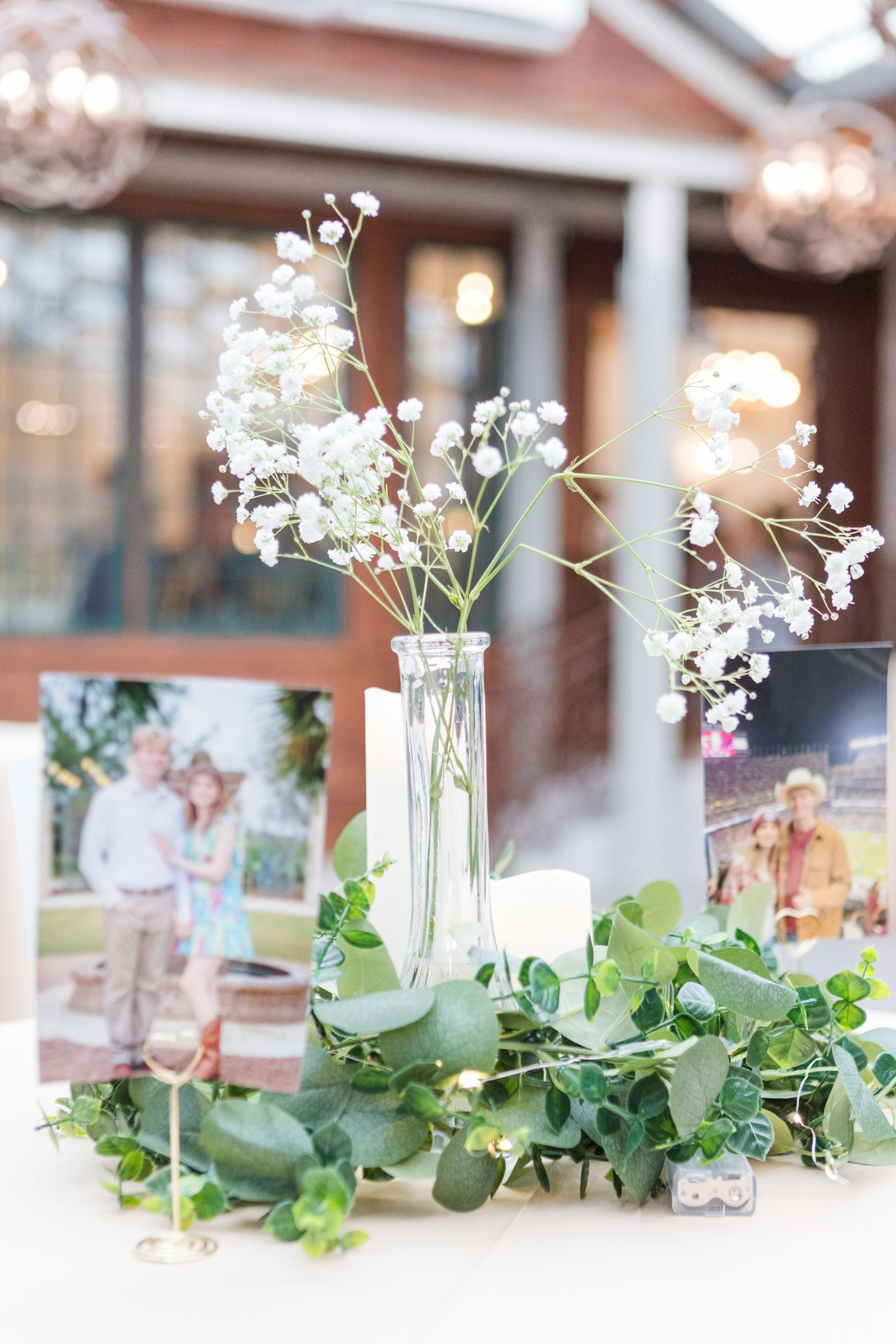 Wedding reception table decor featuring delicate baby's breath flowers in glass vases with eucalyptus garland.