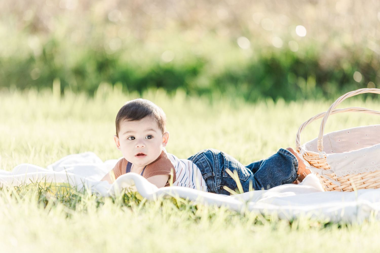 Baby crawling on white blanket in grassy field during sunset photo session.