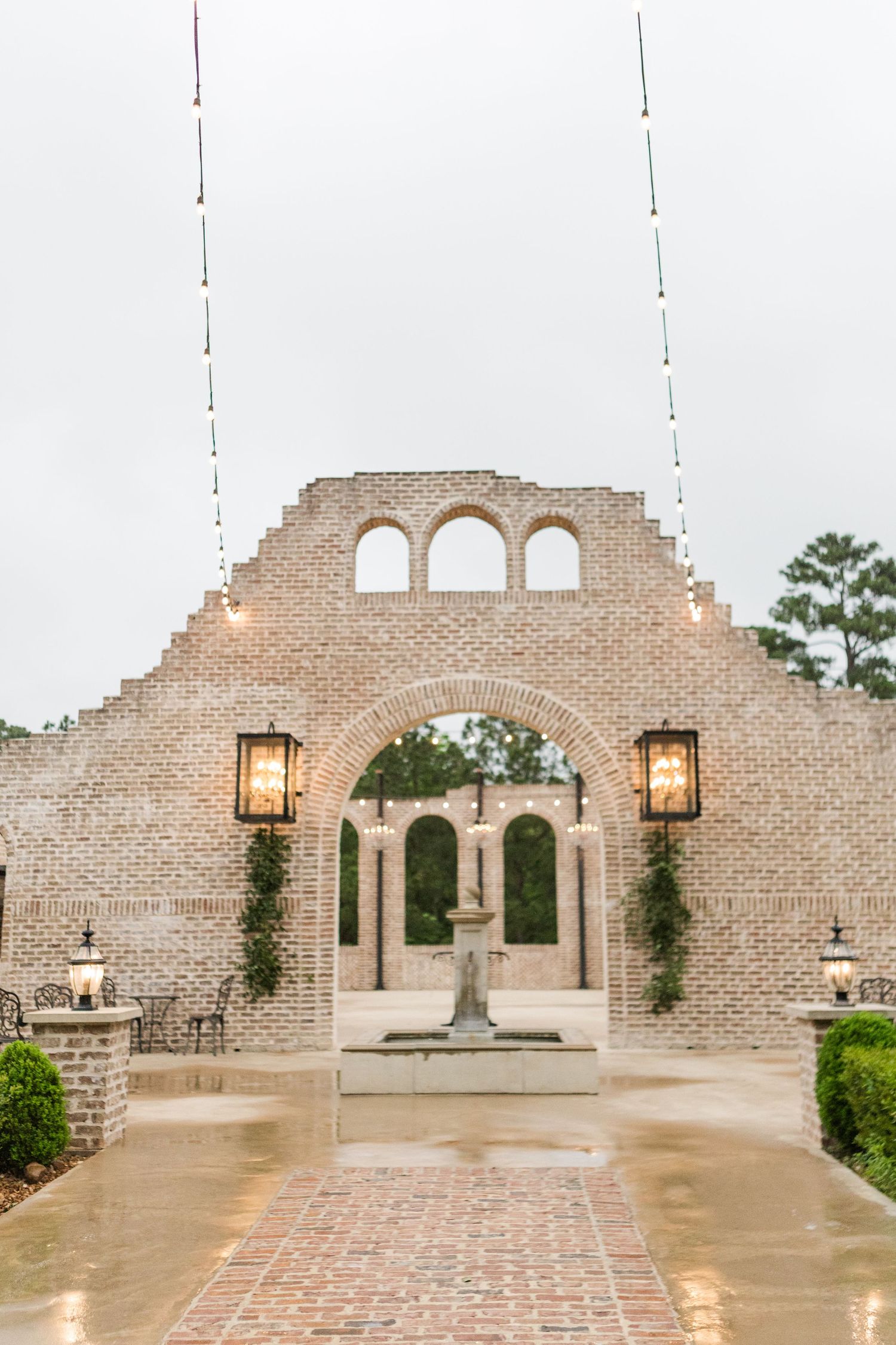 Beautiful brick archway entrance with lanterns and fountain at an upscale wedding venue.