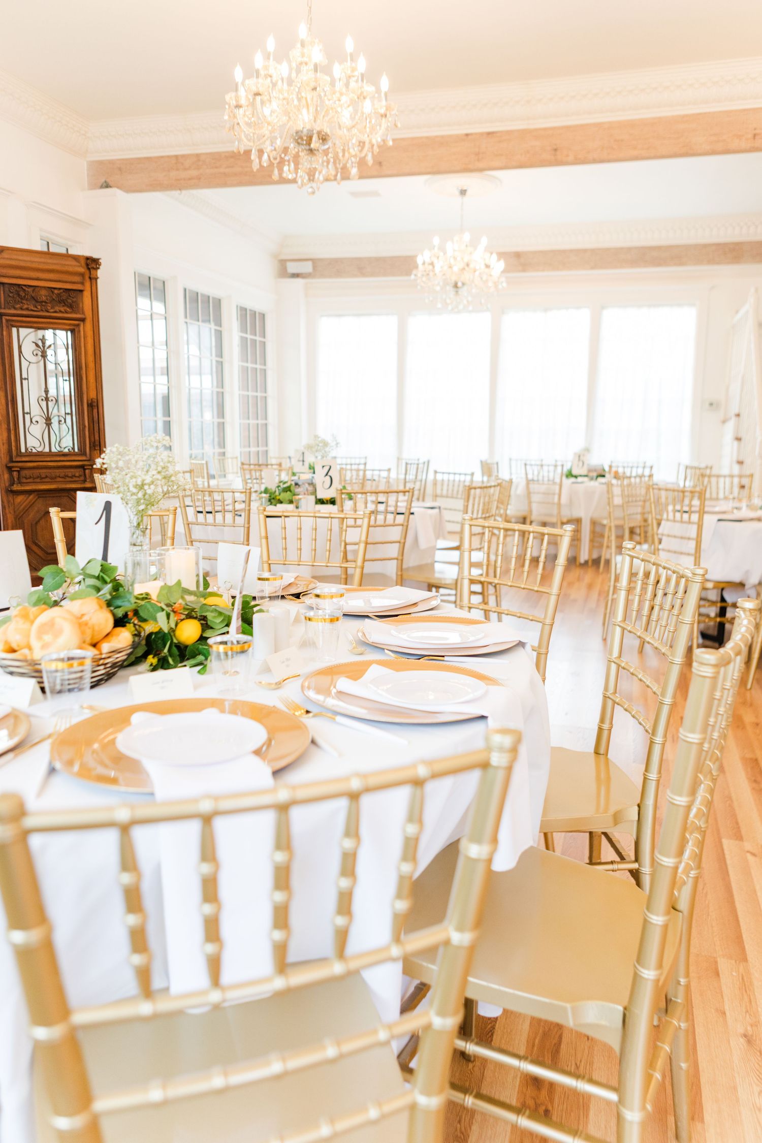 Light-filled wedding reception room with crystal chandelier and gold chiavari chairs.