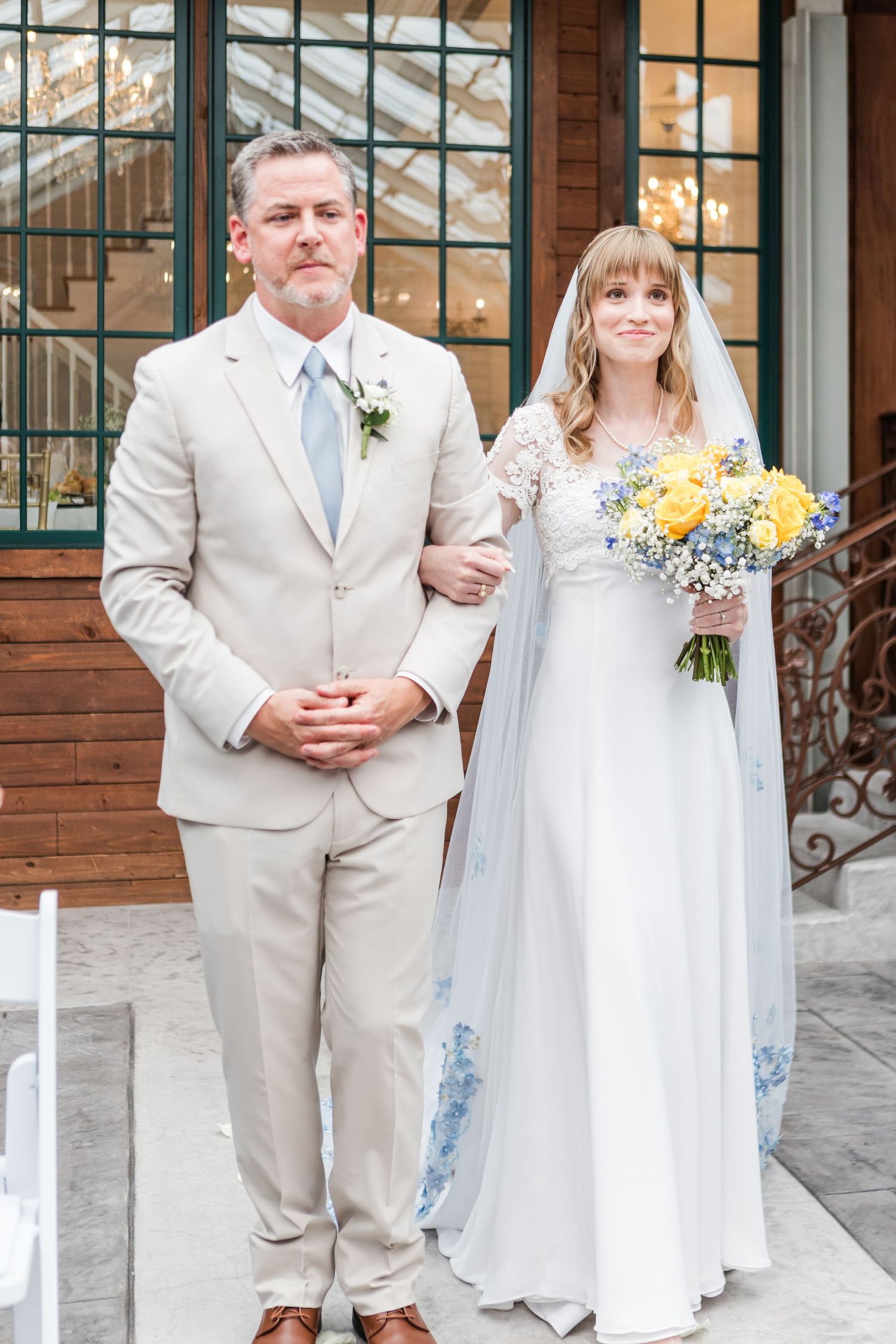 A wedding couple in white and beige attire stand together during their outdoor ceremony.