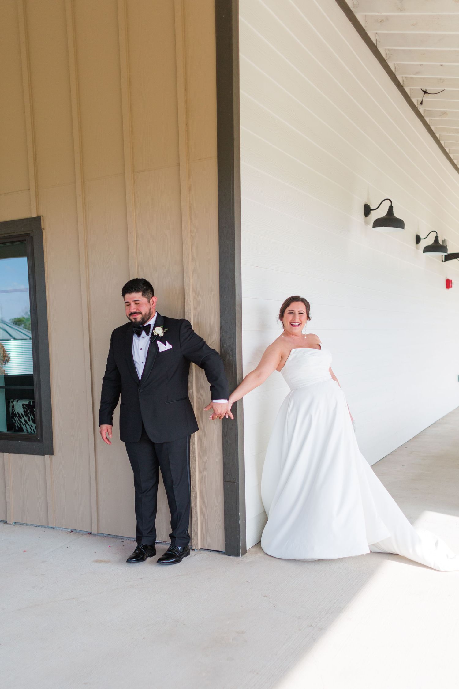 Wedding couple holds hands around corner during playful first look moment.