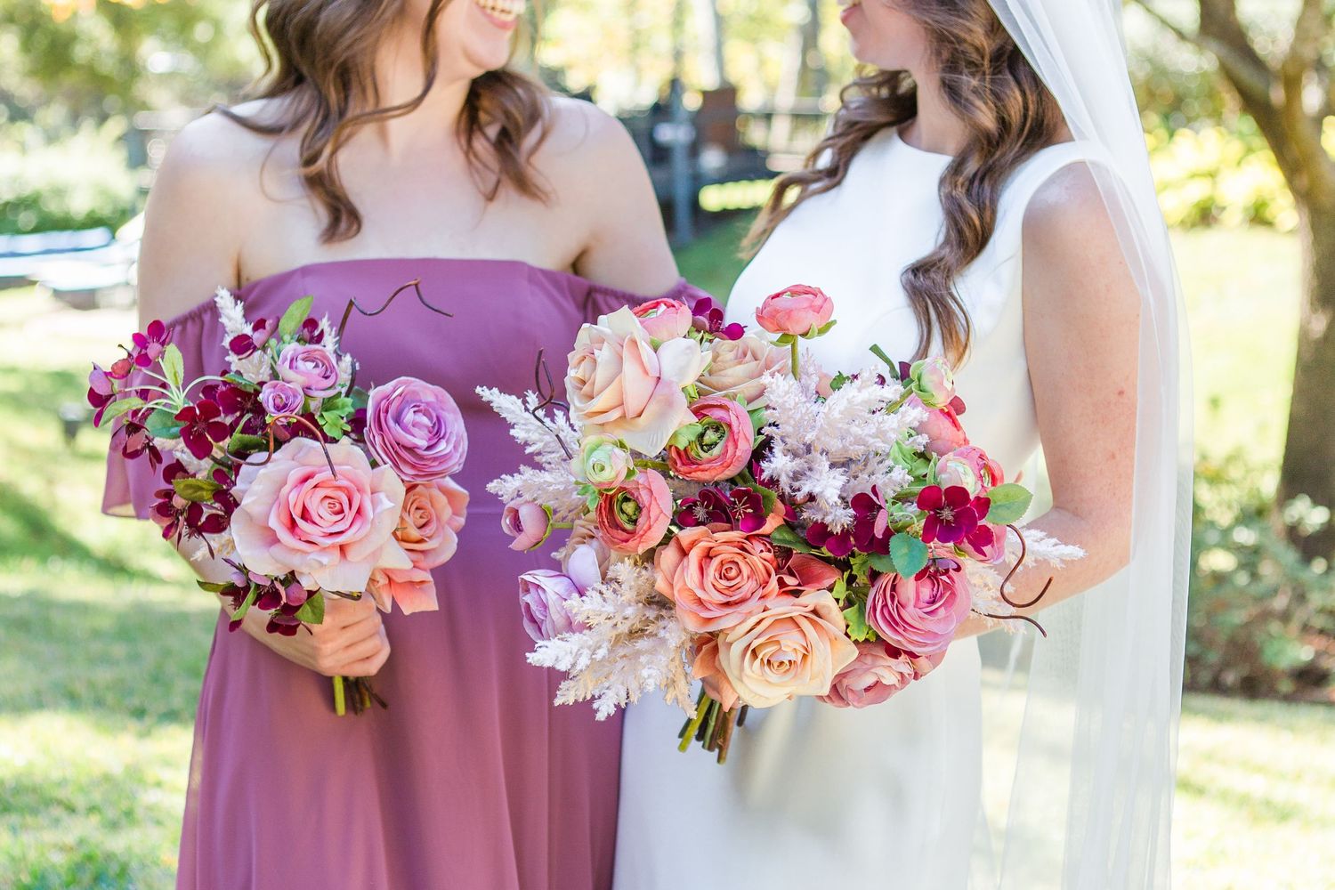 Wedding party members hold vibrant pink and peach floral bouquets during outdoor celebration.