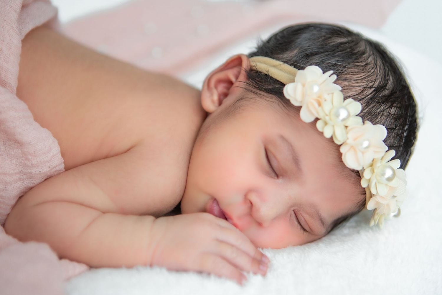 Sleeping baby wearing floral headband during serene photo session.