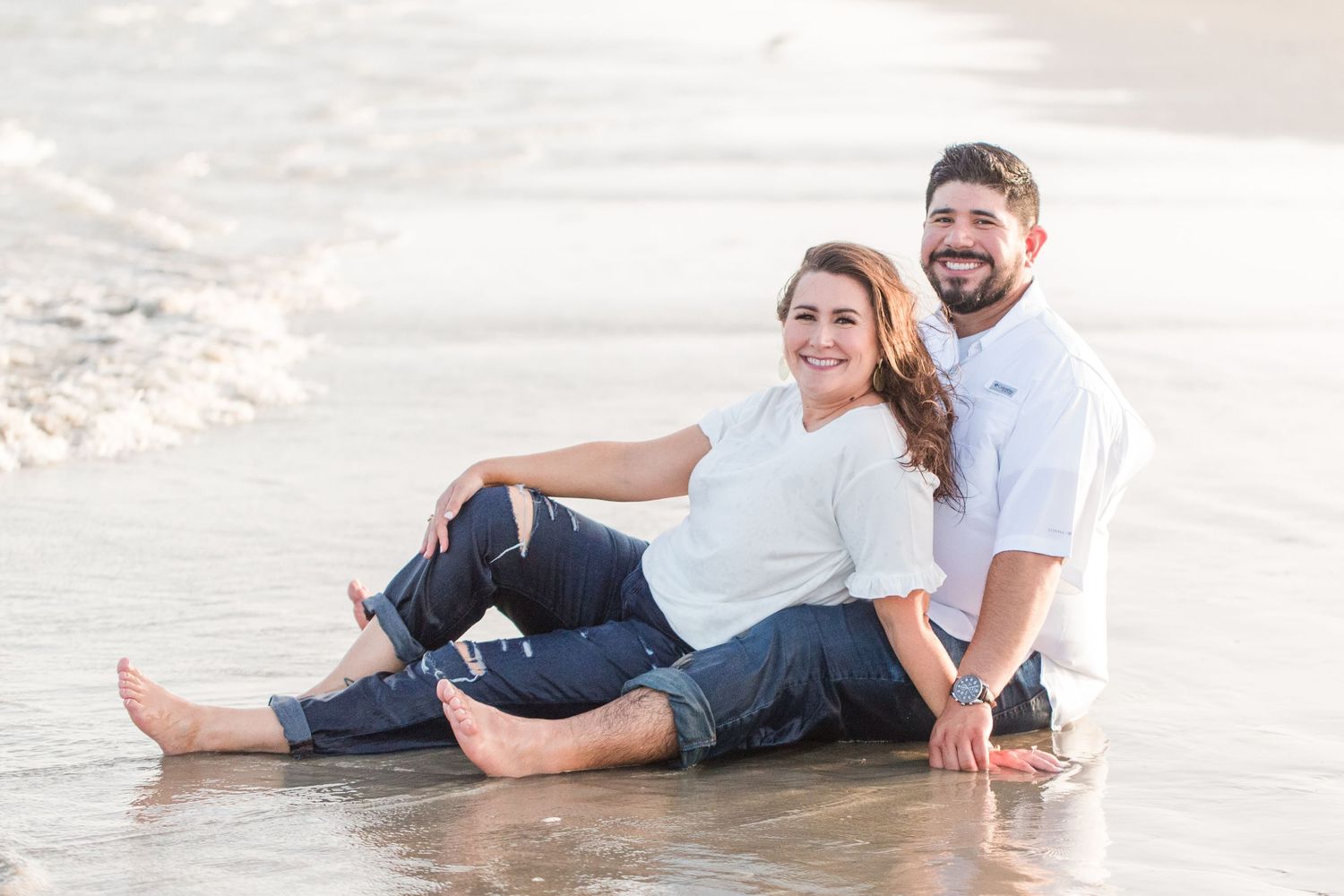 Couple relaxing together on sandy beach during sunset photoshoot.