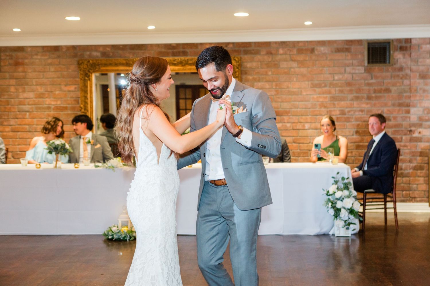 Wedding dance sequence in an elegant brick-walled reception venue with white decor.