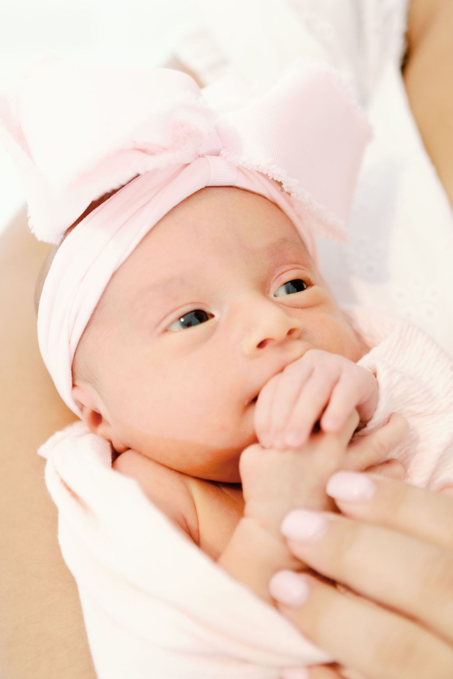 Close up view of a newborn baby in soft pink swaddle getting massaged by gentle hands.