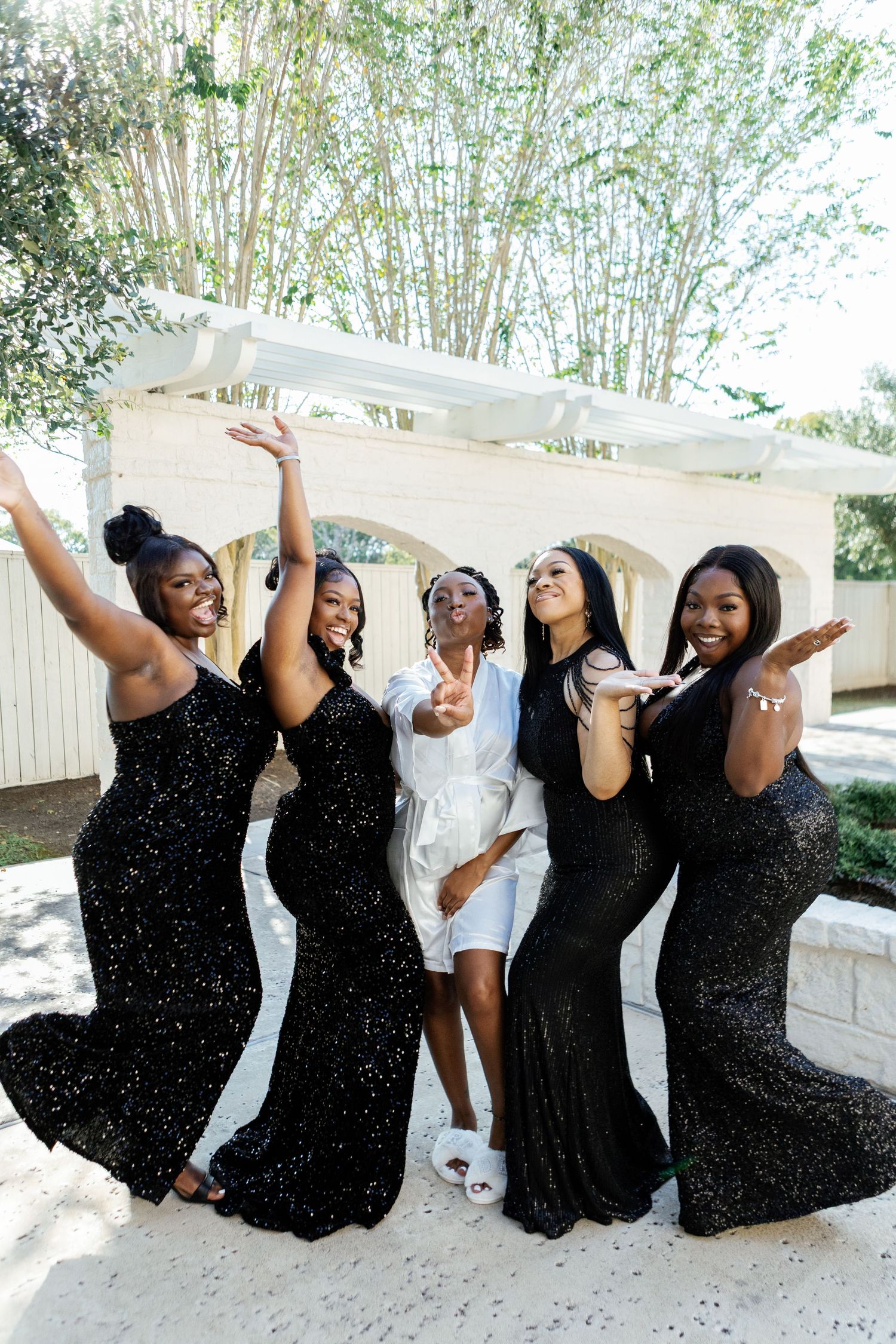 Group in black outfits poses joyfully against white architecture background.