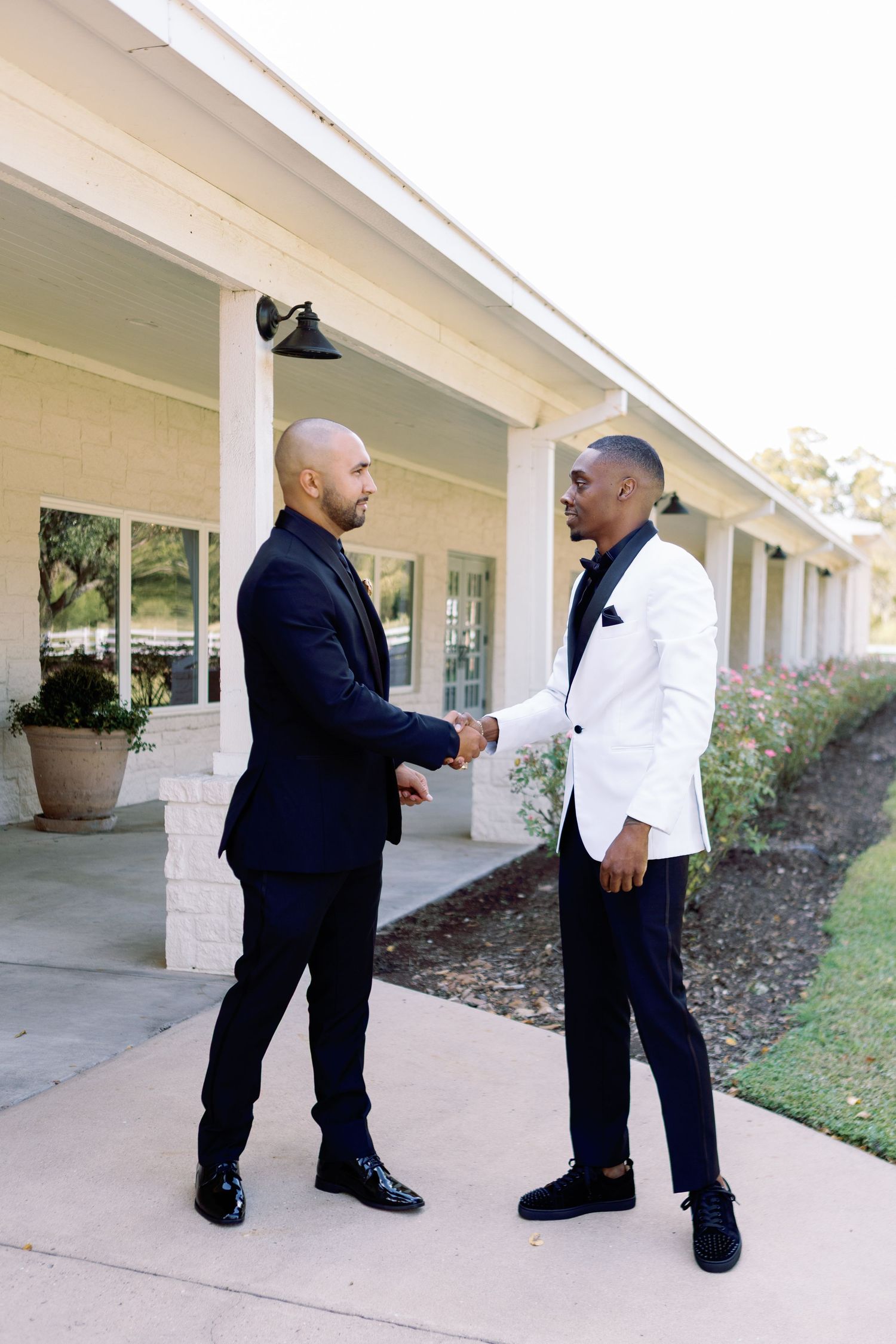 Groomsmen in formal attire greet each other outside a white columned building.