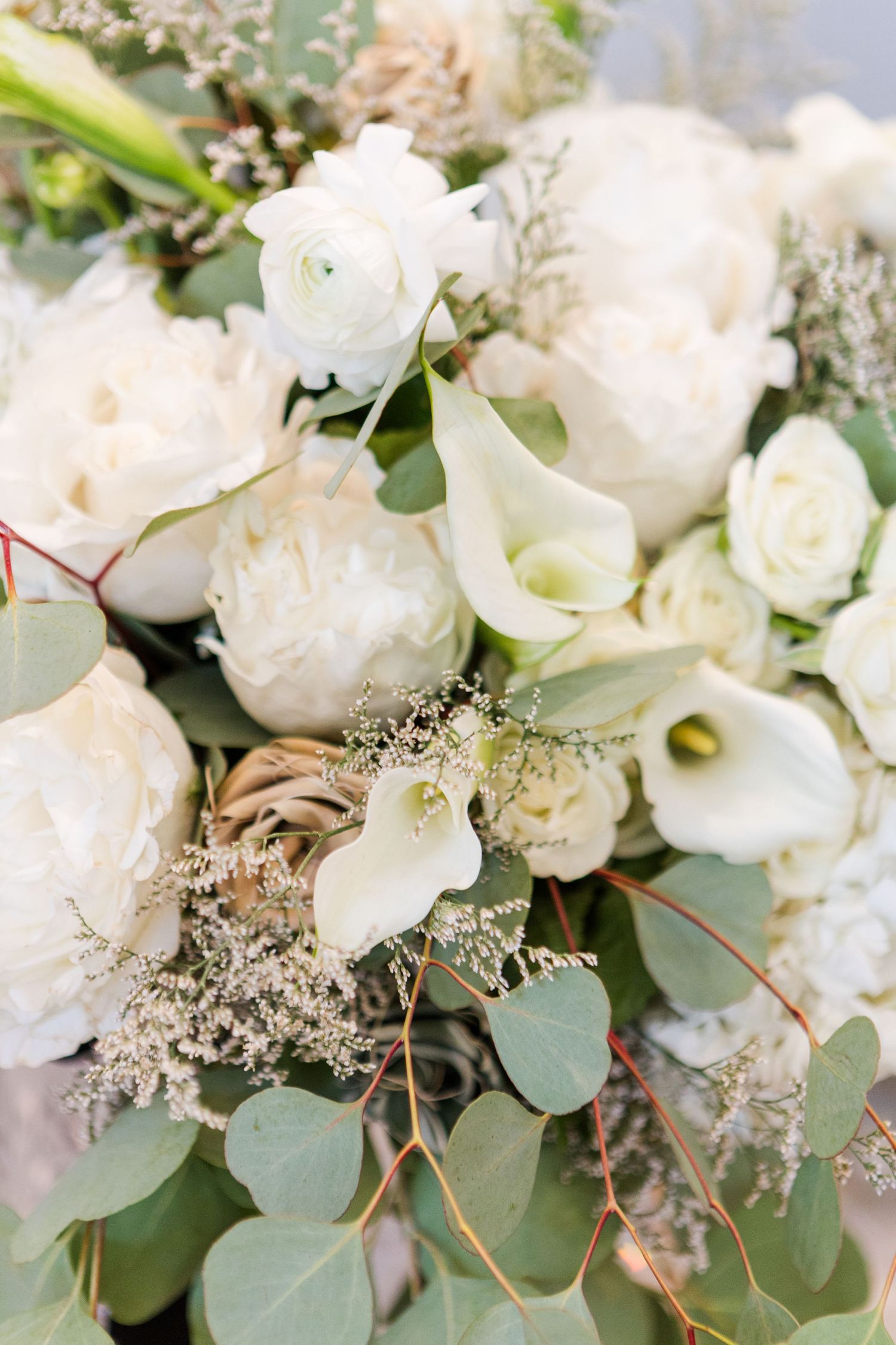 A close-up view of a white floral arrangement featuring roses and eucalyptus leaves with delicate baby's breath accents.