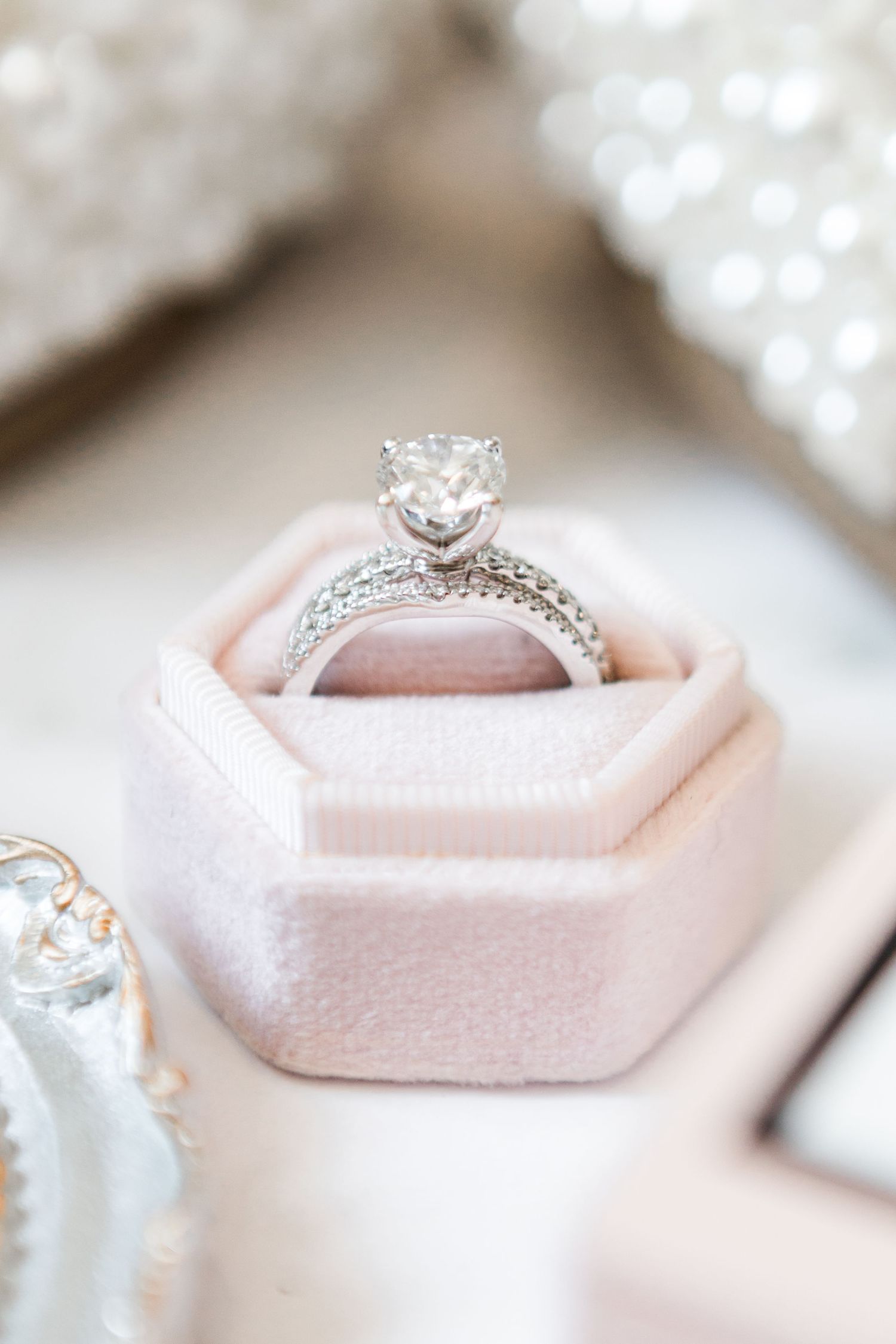 Close-up view of an elegant diamond engagement ring nestled in a blush pink hexagonal display box.