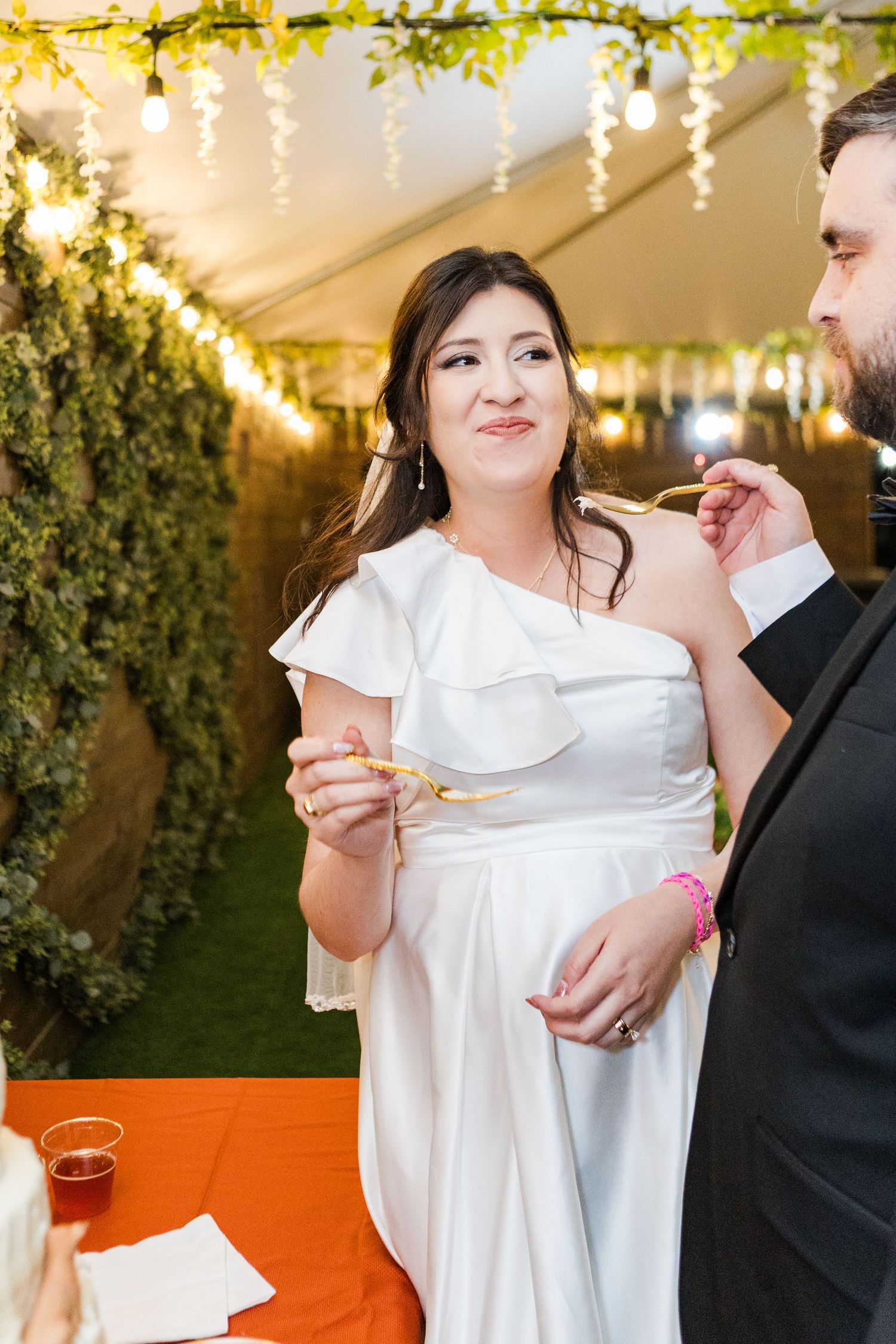 Wedding reception under string lights with white decor and orange table linens.