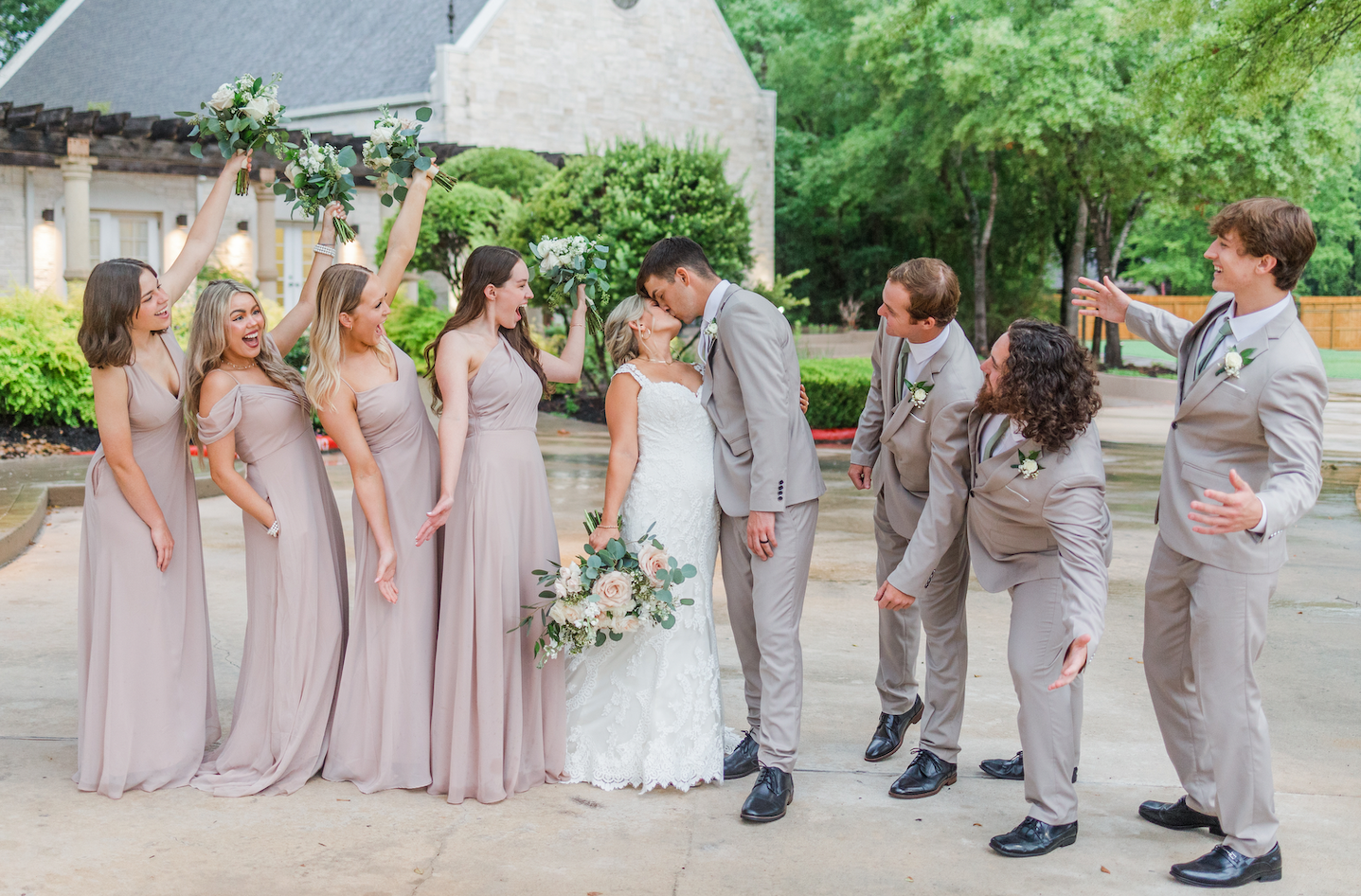 Wedding party in pink dresses and gray suits poses for group photos outdoors.