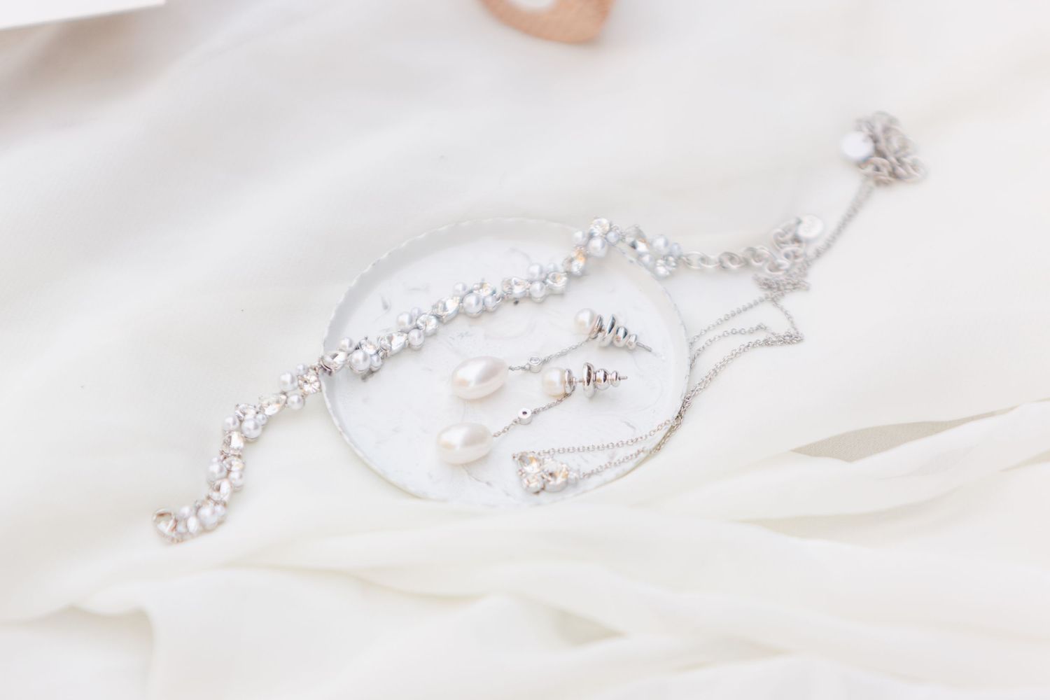 Delicate silver jewelry and accessories displayed on white silk fabric.
