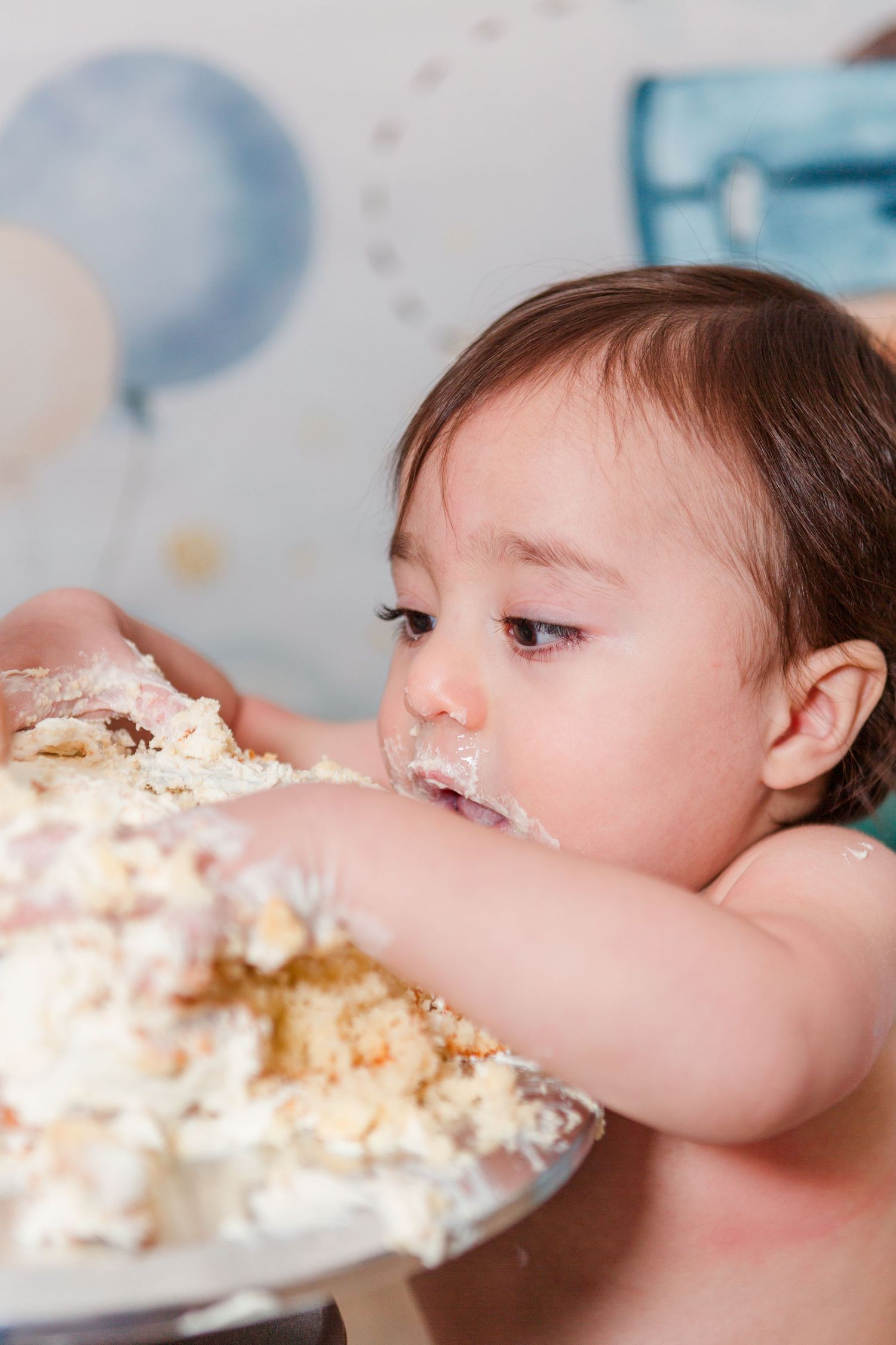 Baby enthusiastically eating white birthday cake during cake smash session.