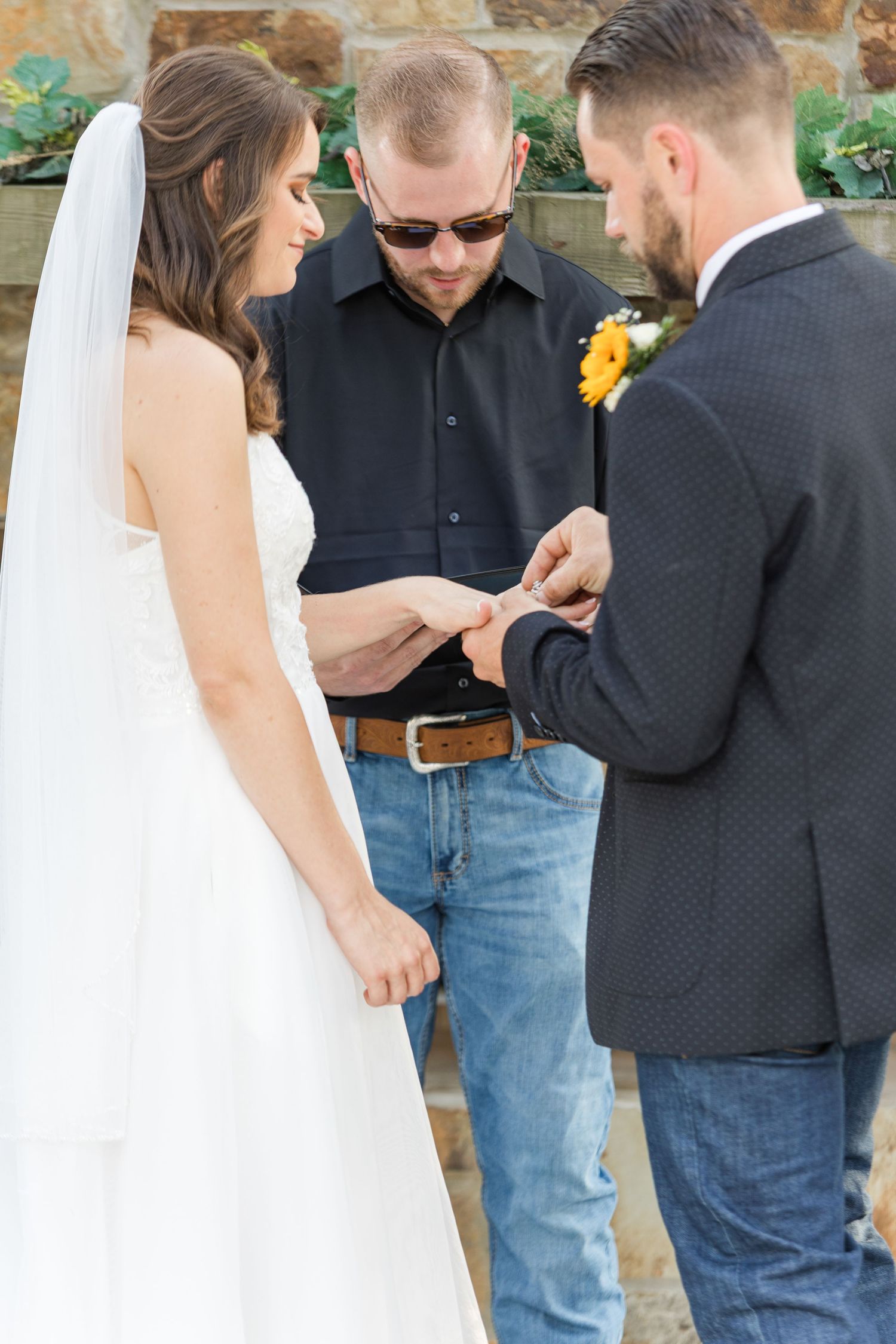 Wedding ceremony details with wedding rings and white dress against stone wall background.