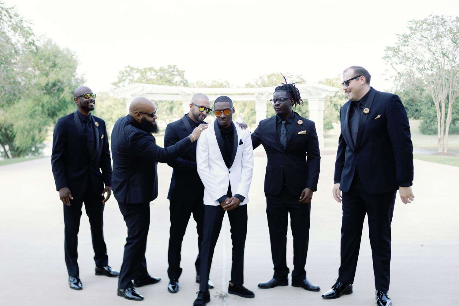 Wedding party in formal black attire poses creatively outdoors.