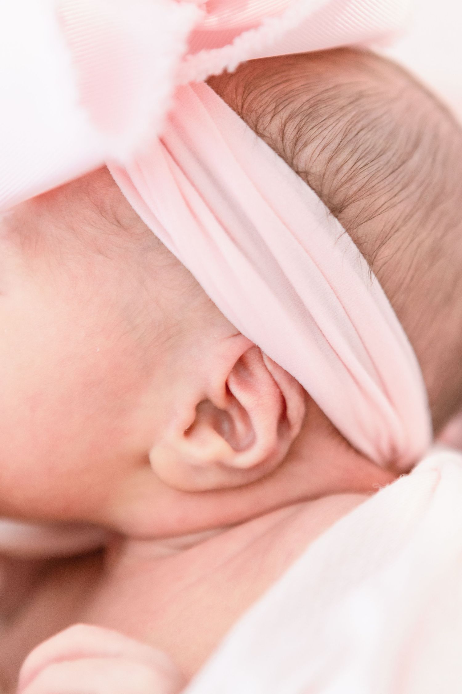 Close up shot of a tender newborn baby's ear wrapped in soft pink fabric.
