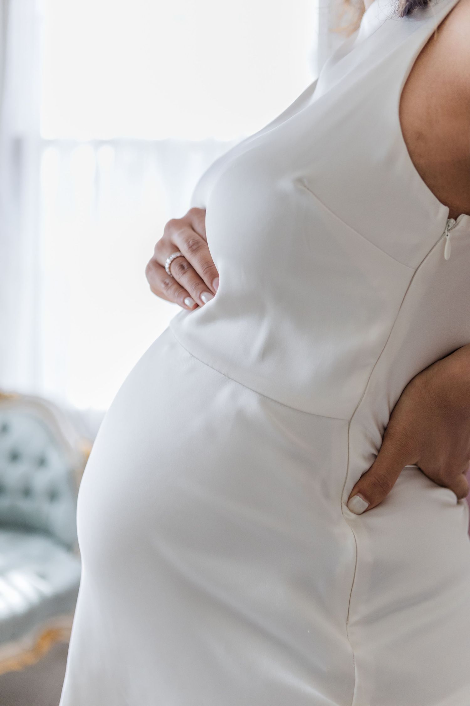 Close-up details of elegant white maternity dress in studio setting.