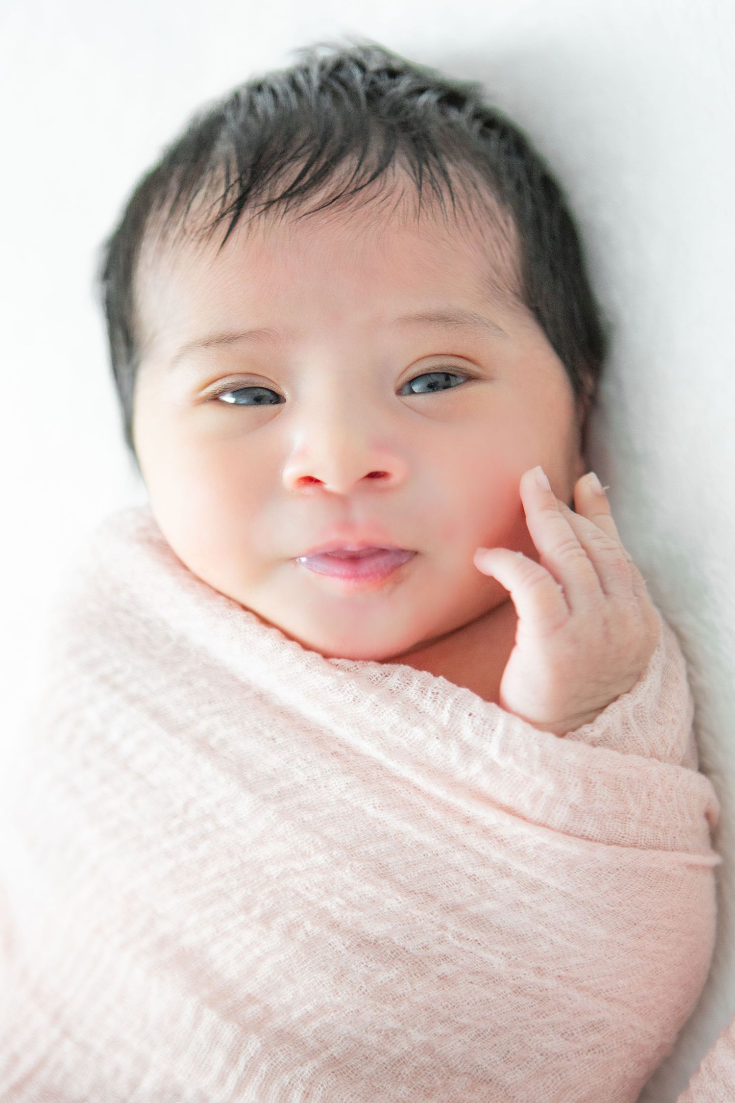 Sweet close-up portraits of a baby wrapped in soft pink blanket.