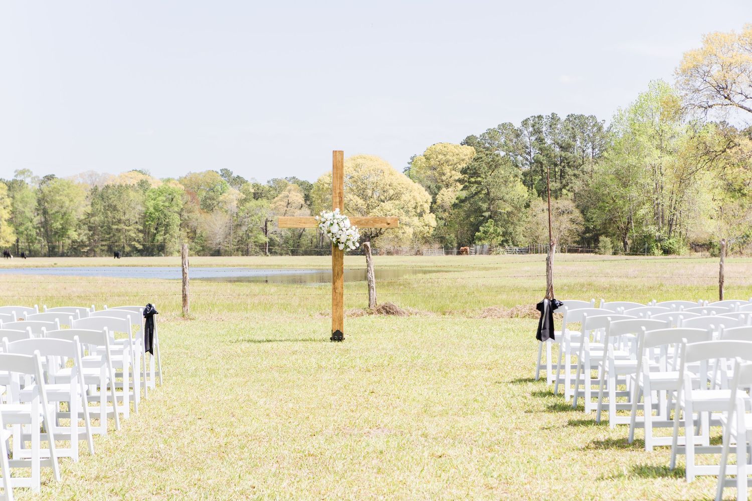 Rows of white chairs set up outdoors for a wedding ceremony with trees in the background.