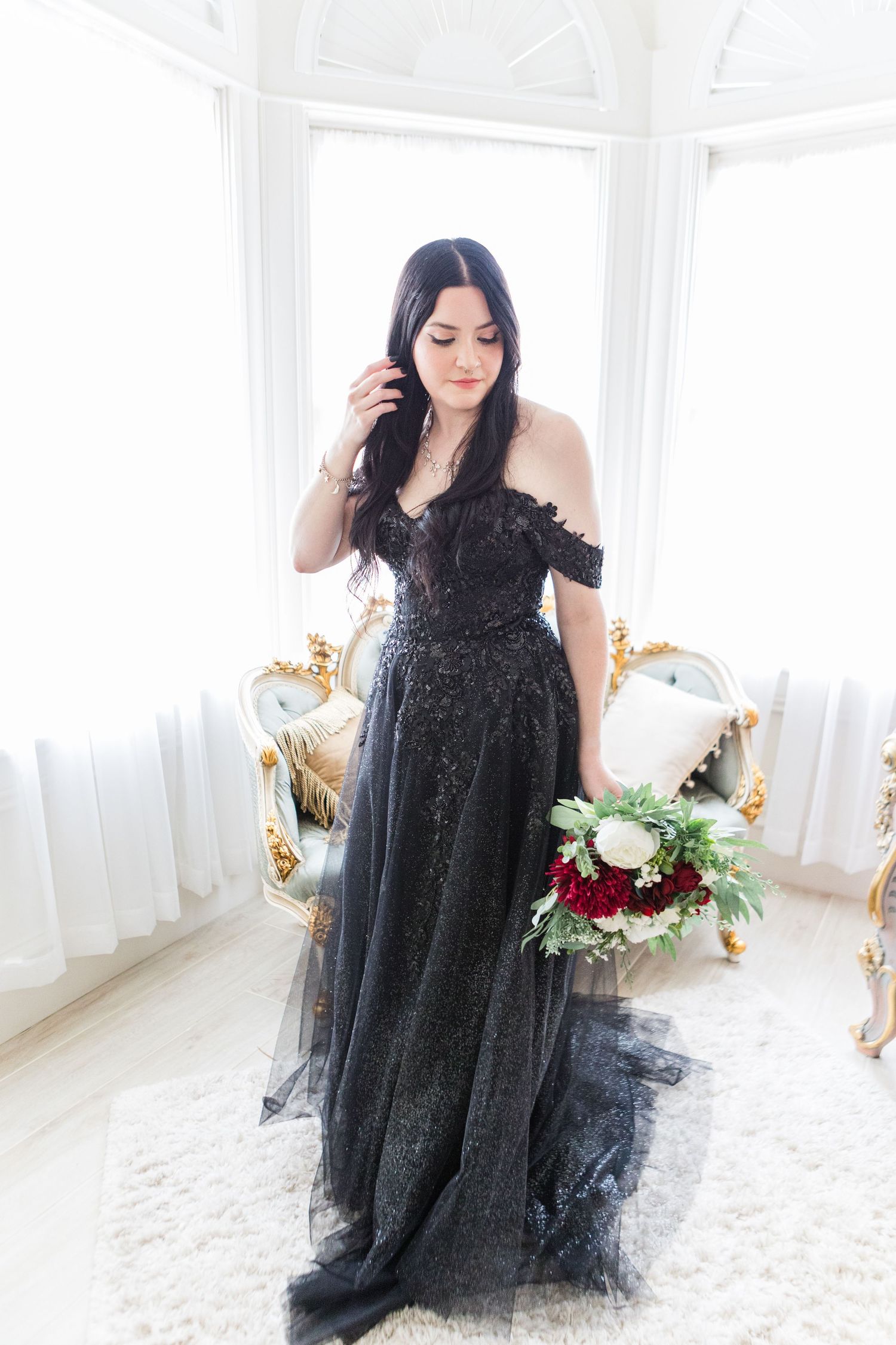 Model in black tulle gown poses gracefully in bright white room with ornate gold furniture.