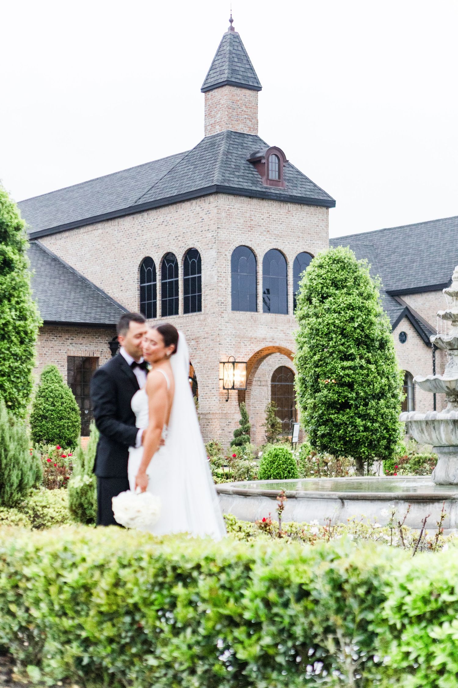Romantic moment captured in front of a beautiful stone chapel with manicured gardens.