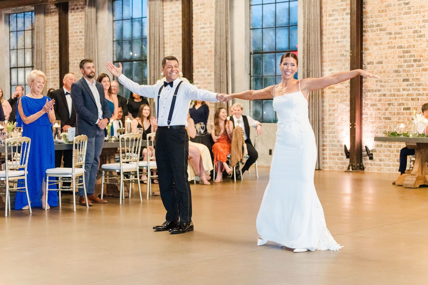 Wedding celebration in a spacious brick venue with couples dancing and guests watching from tables.