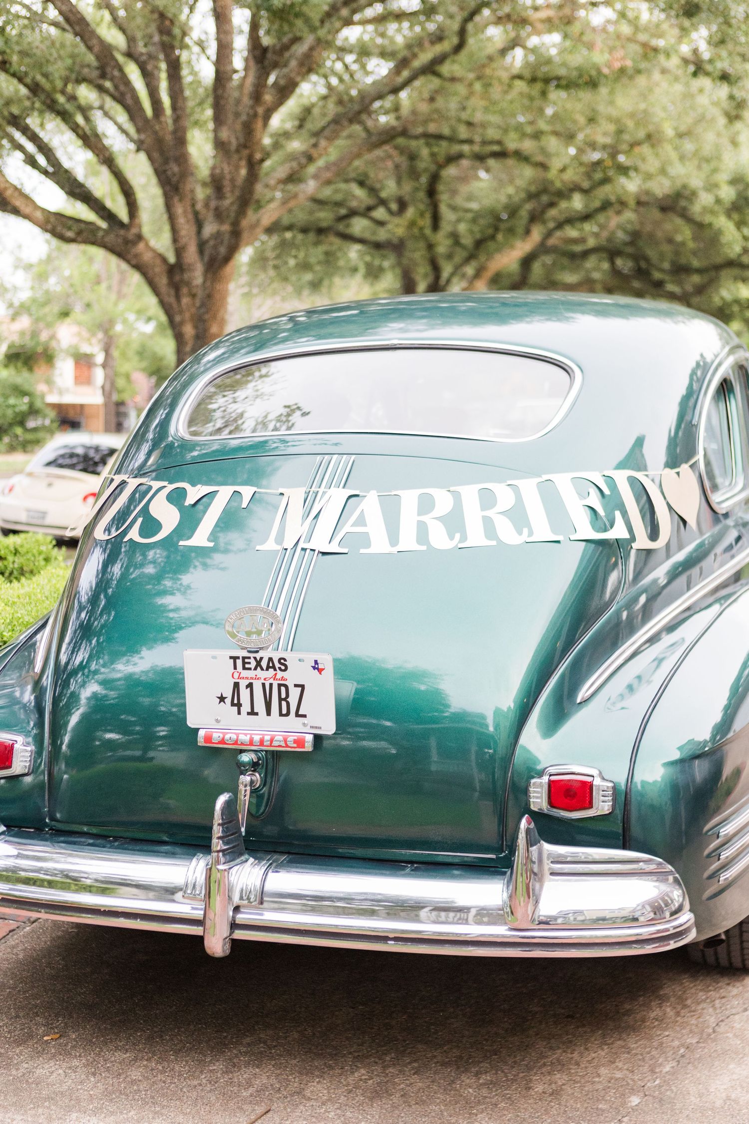 Vintage green car with Just Married sign and Texas license plate parked under trees.