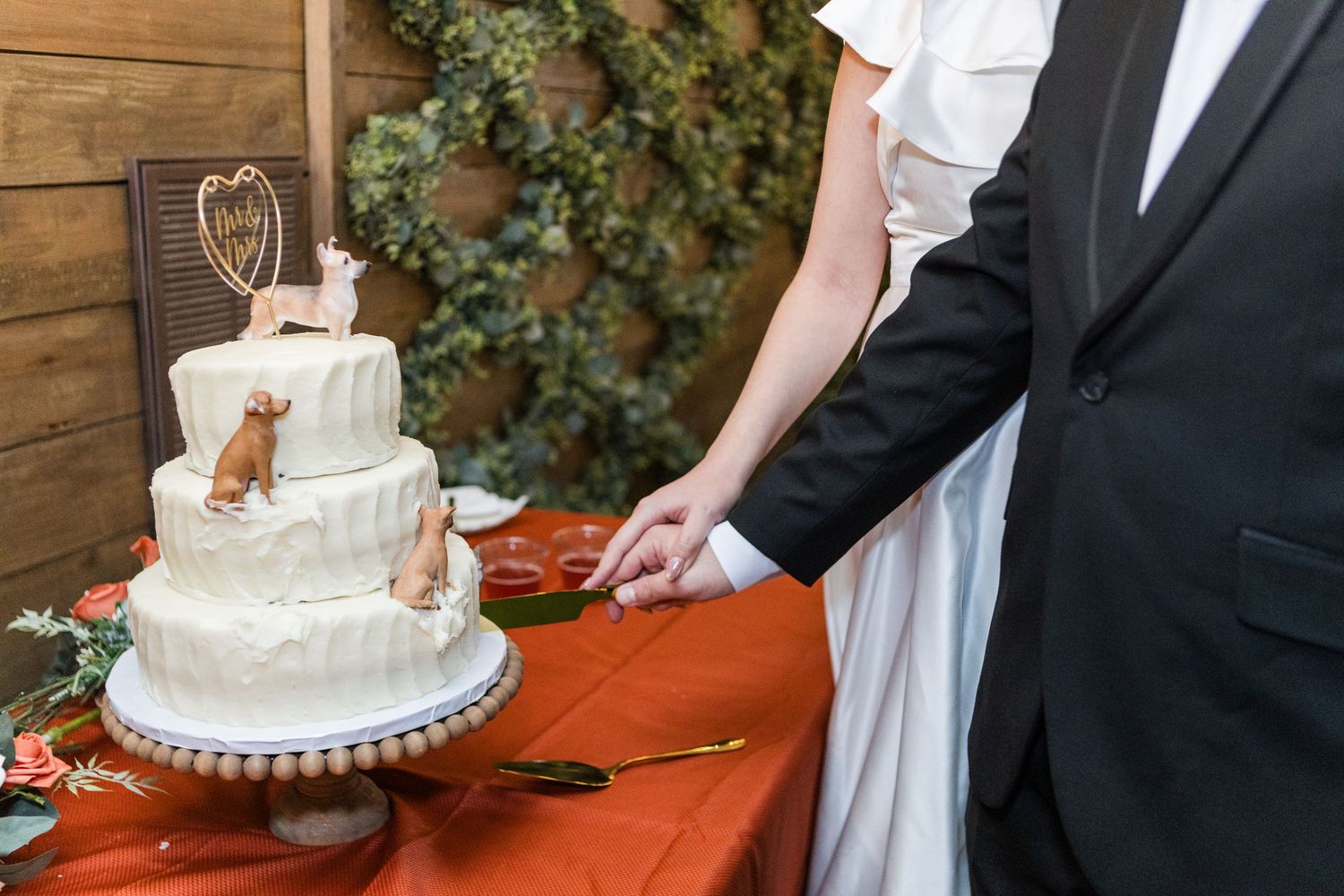 Wedding cake cutting ceremony with elegant white tiered cake on orange tablecloth.