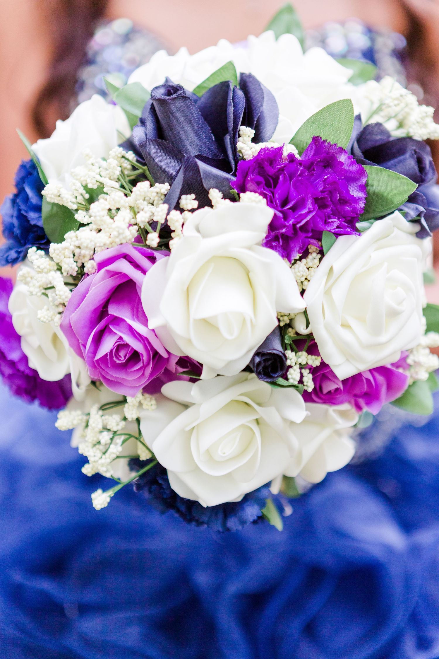 Purple and white rose bouquet resting on royal blue fabric.