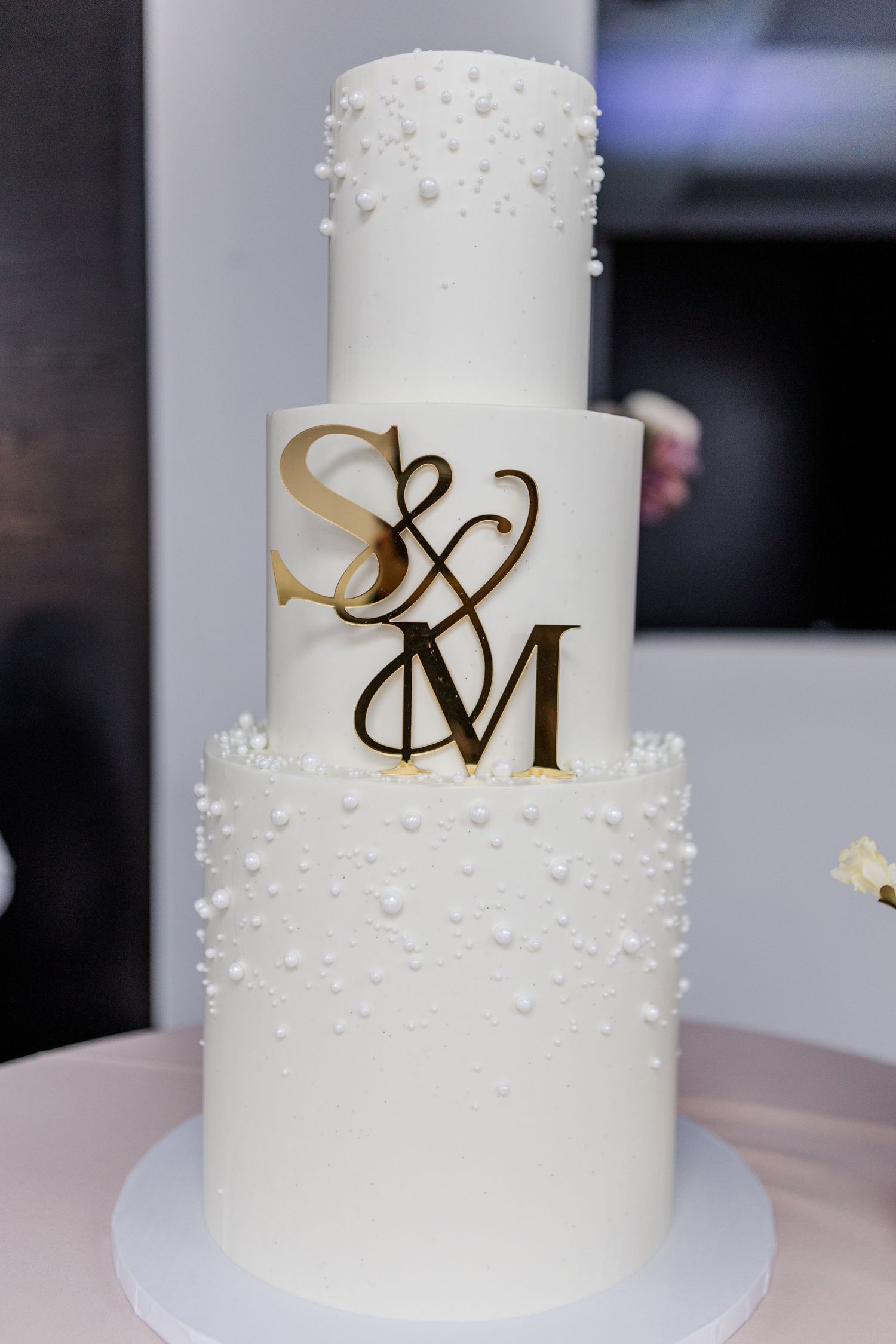 White wedding cake decorated with pearl details and metallic monogram initials.