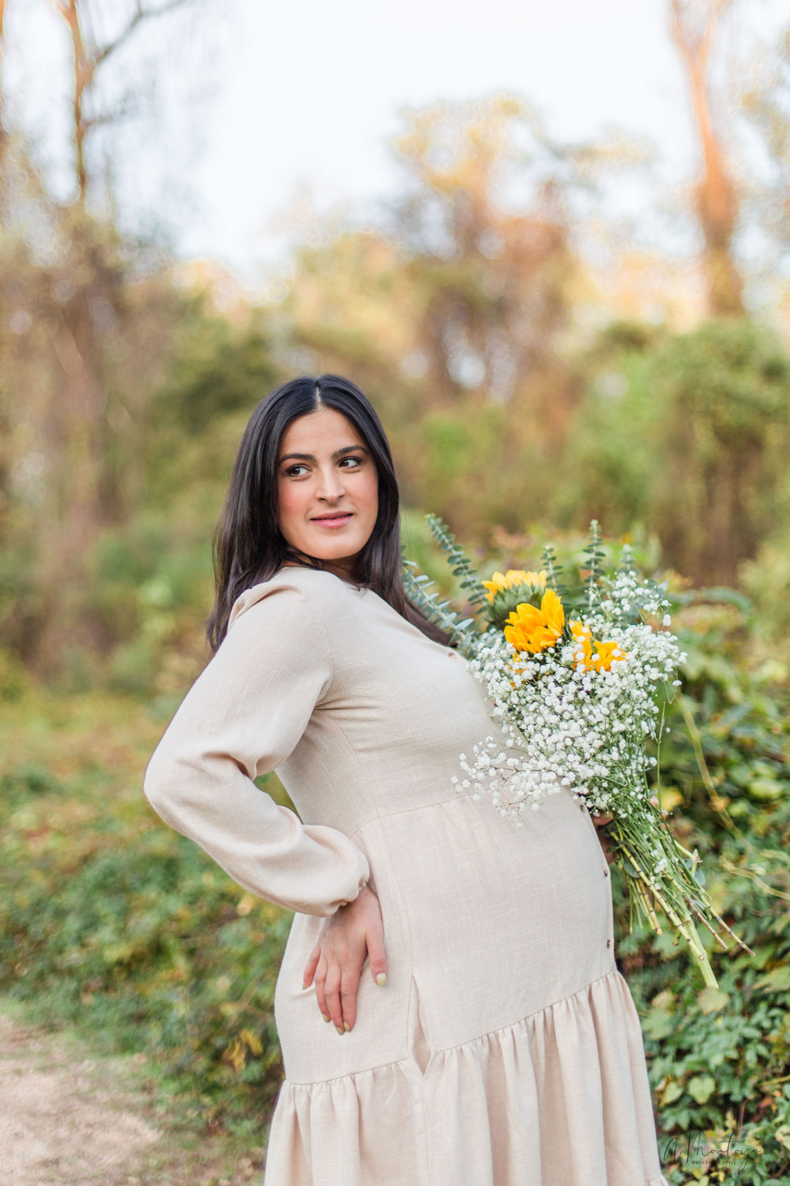 Person in cream dress holding wildflowers outdoors in autumn scenery.