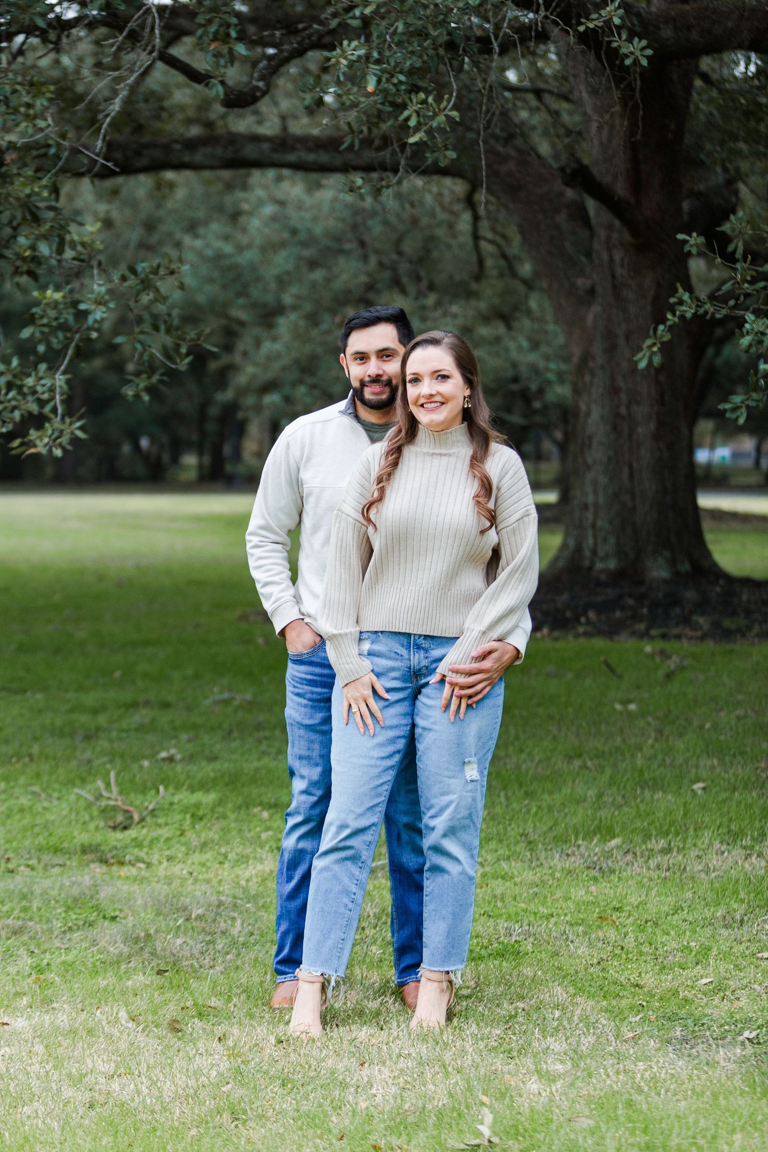 Couple in coordinated cream sweaters and jeans pose outdoors.