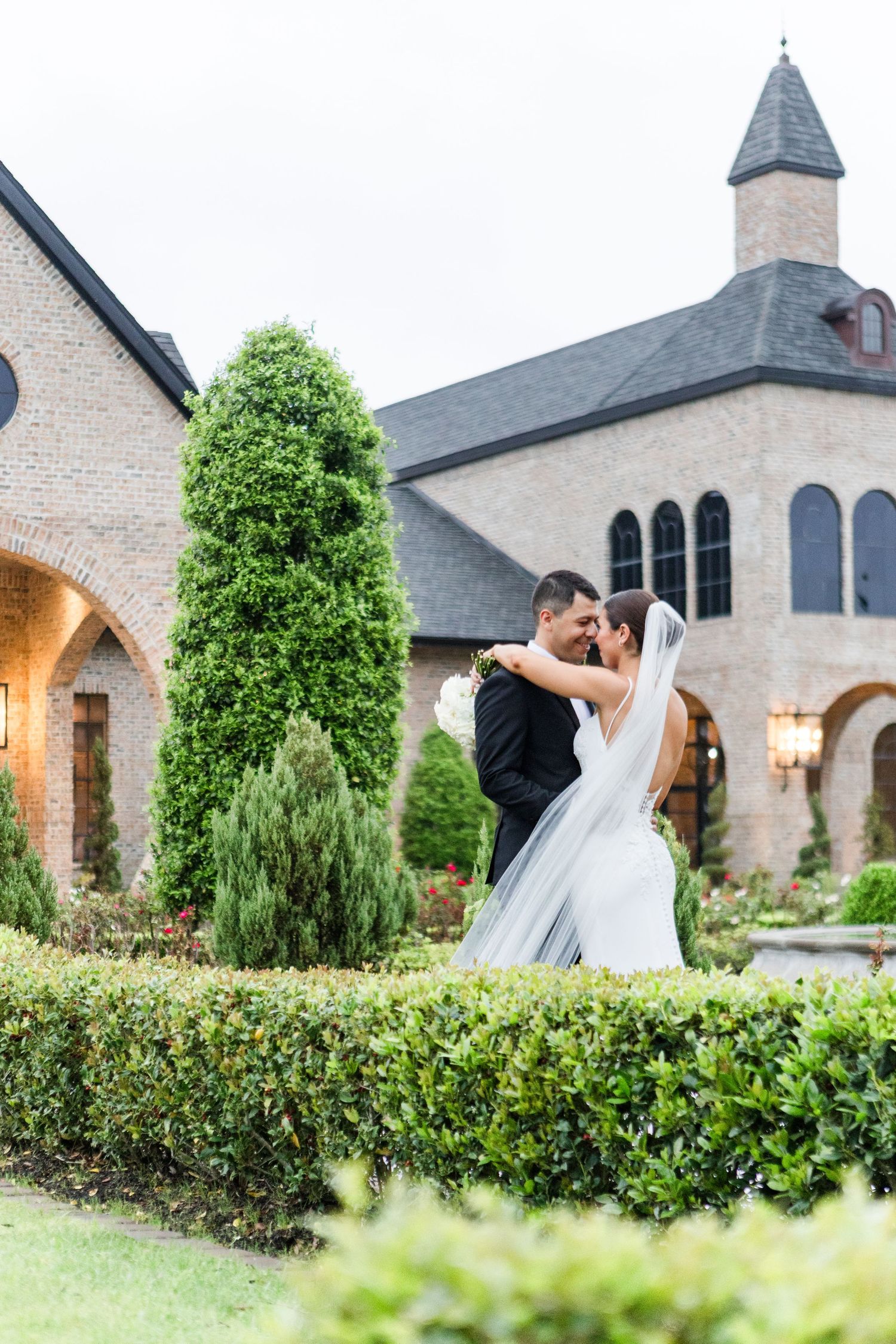 Tender embrace captured in front of a stone chapel surrounded by beautiful landscaping.