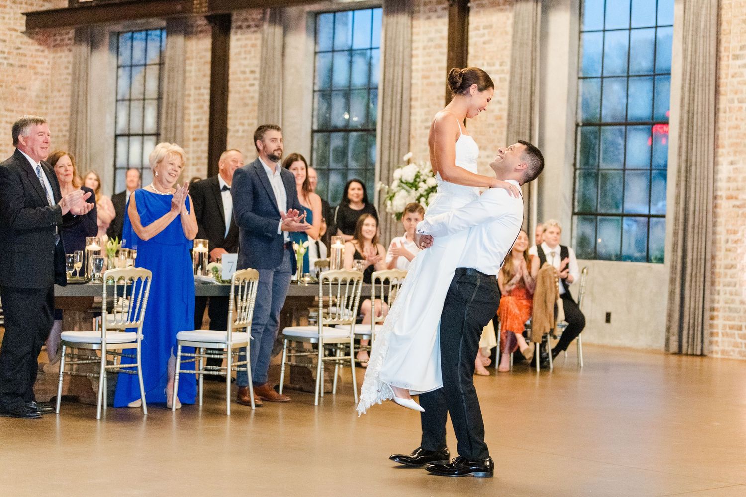 Wide shot of wedding guests dancing and celebrating in an industrial-style reception space.