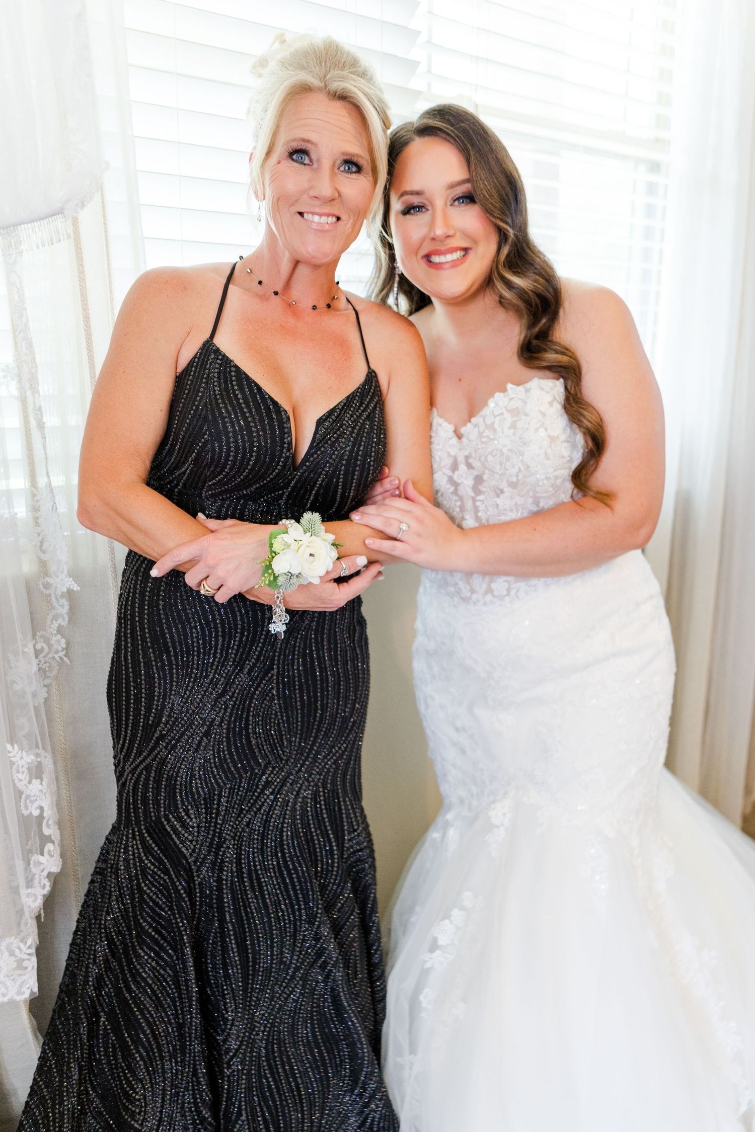 Two women in formal dresses, one in white and one in black, posing together at a wedding.