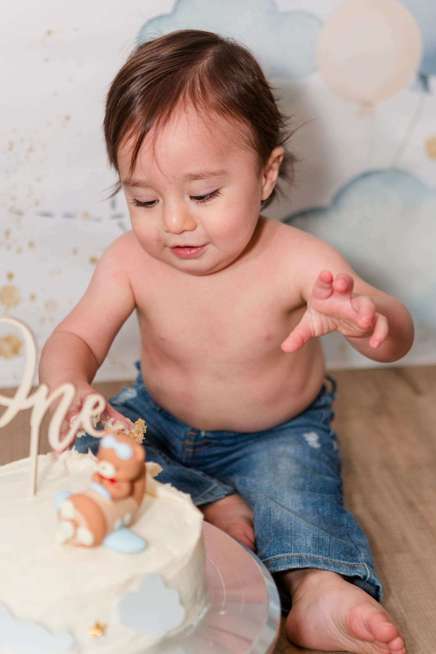 Cake smash photo session with small toys and frosting on wooden floor.