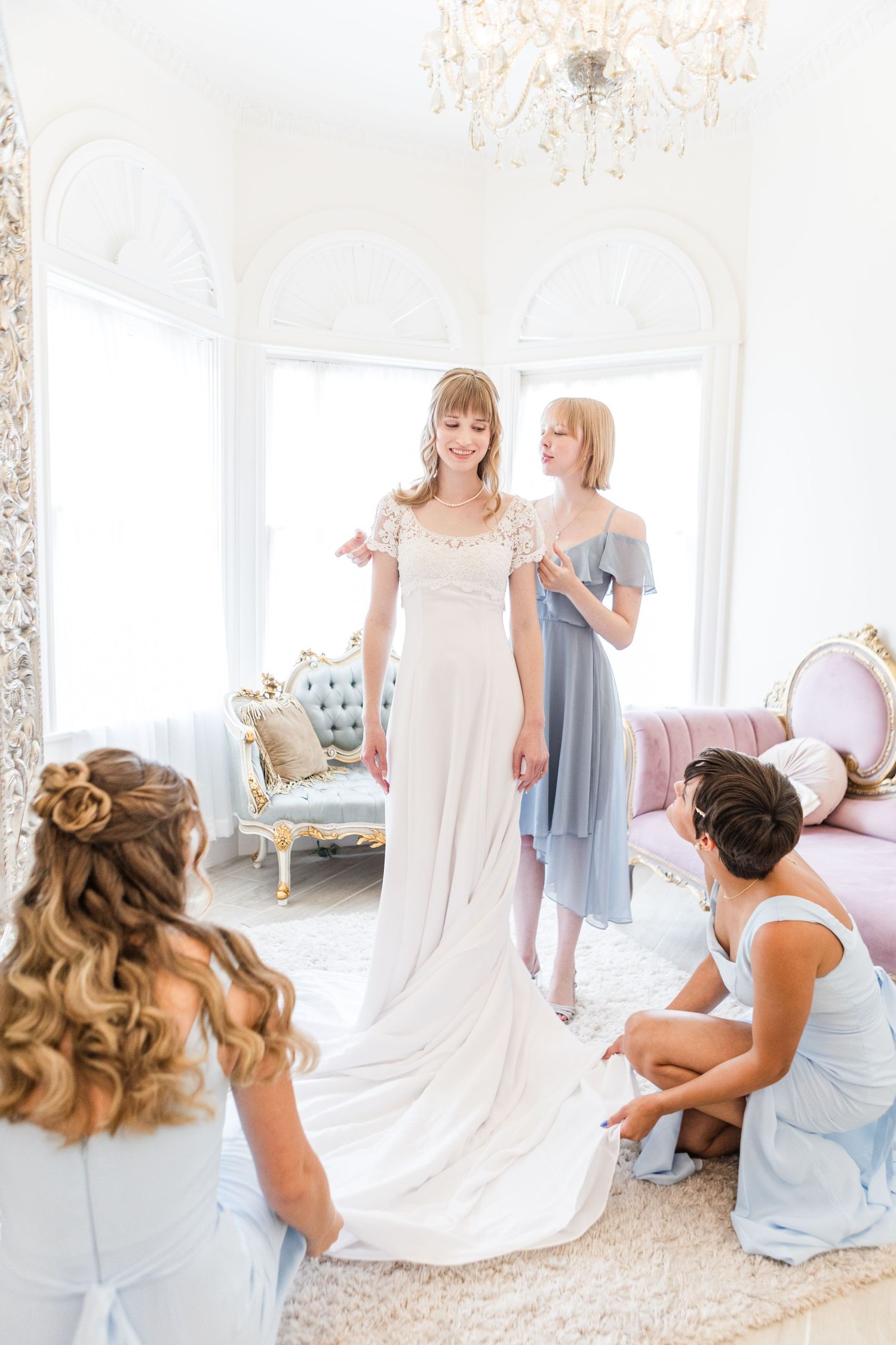 Wedding preparation moments captured in a luxurious white room with chandelier.