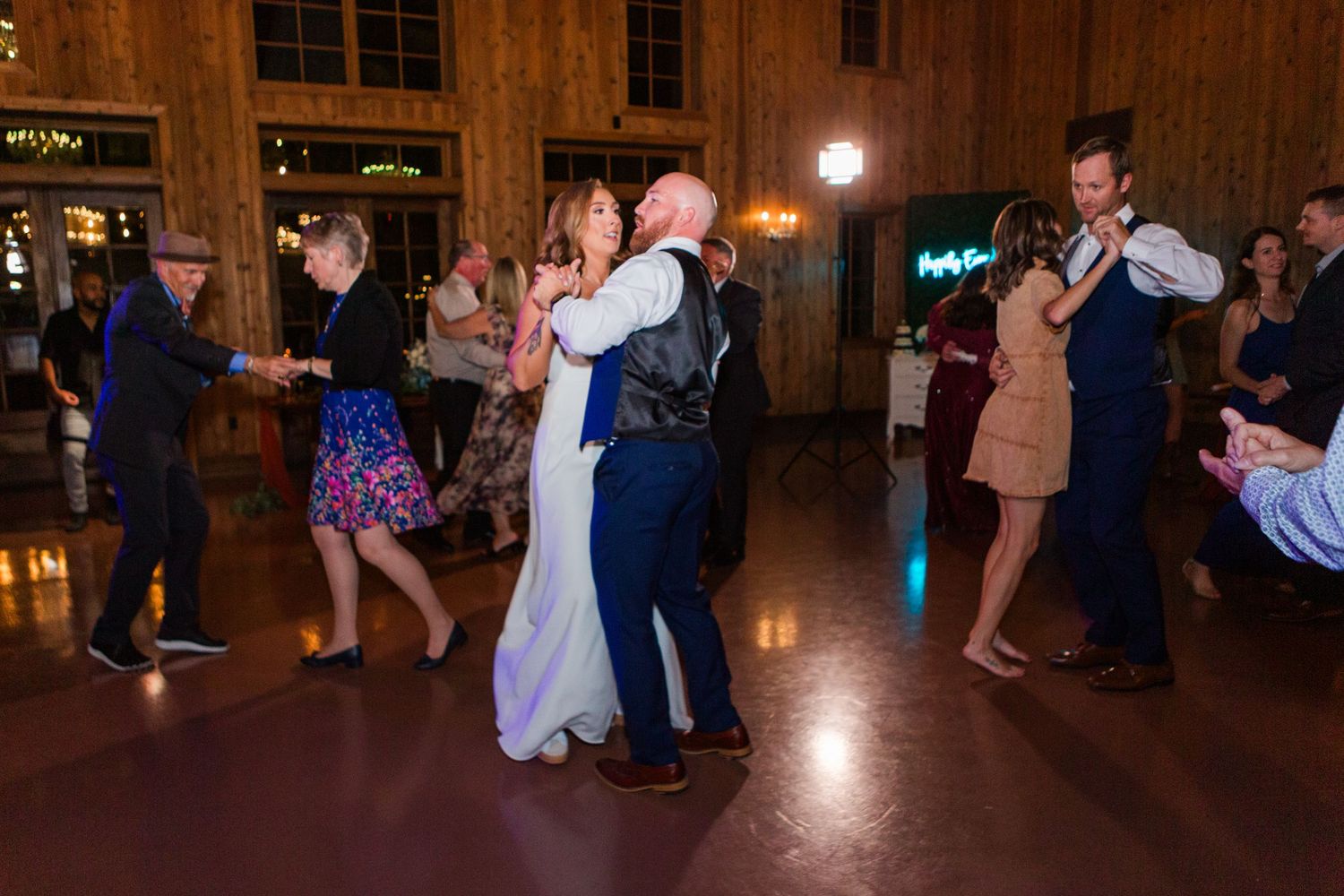 Wedding guests dancing on a rustic wooden dance floor with warm lighting.
