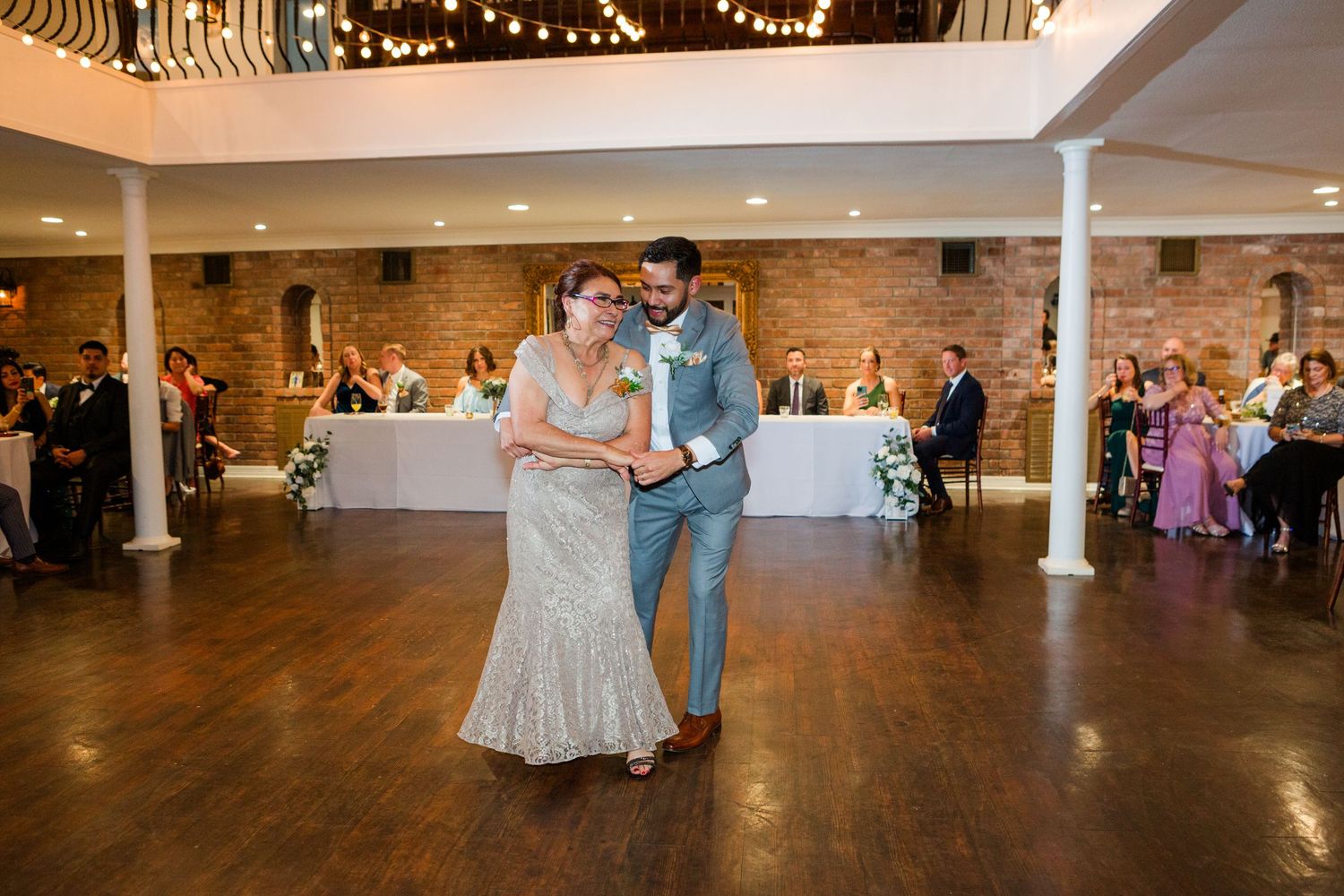 Panoramic view of wedding reception dance floor with string lights overhead.