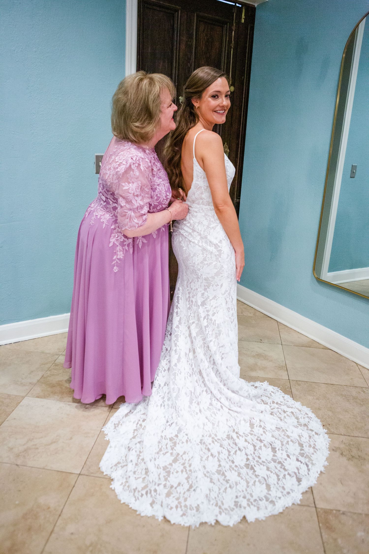 A stunning lace wedding gown with flowing train on display in a blue-walled room.