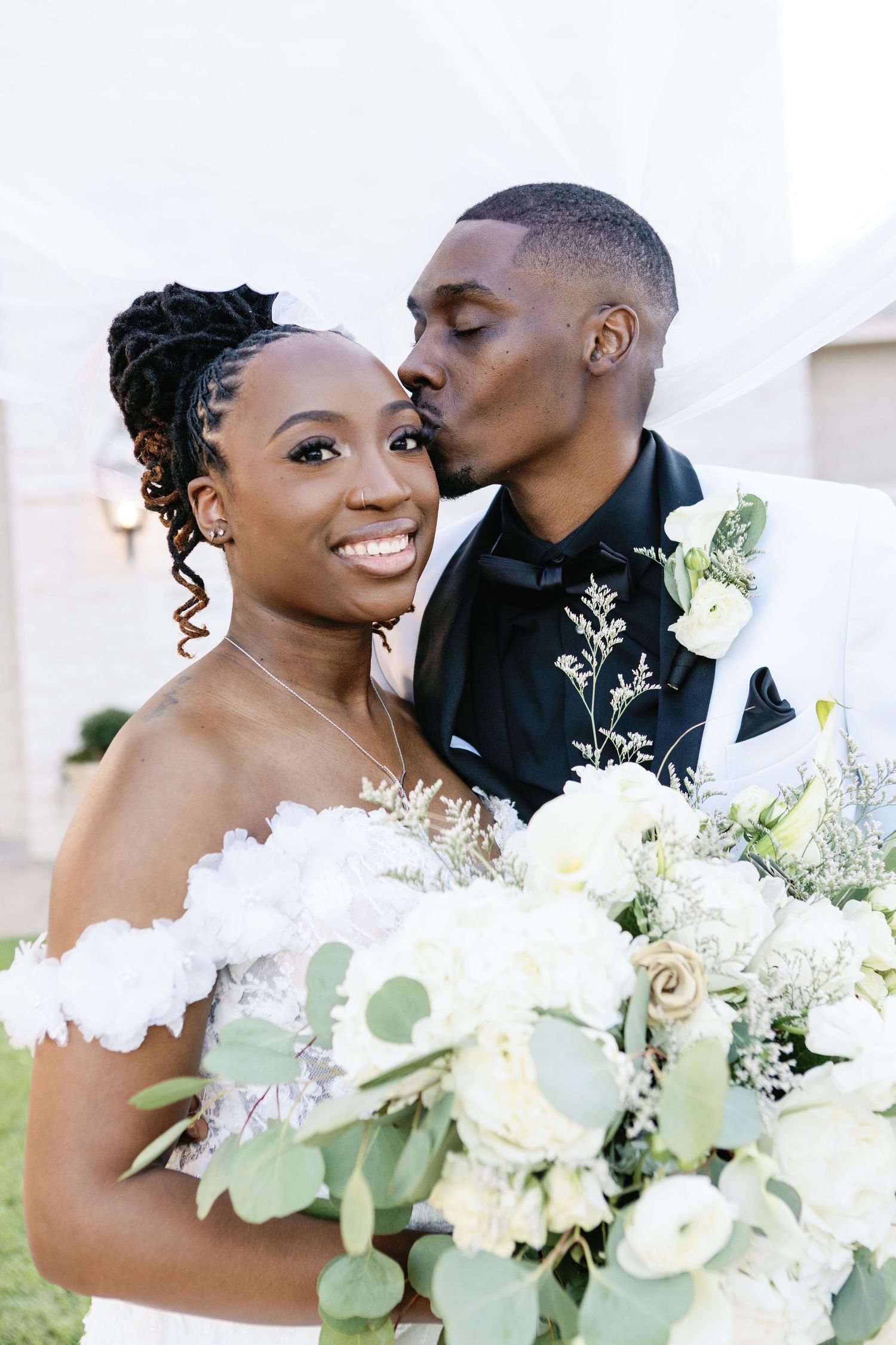 Beautiful wedding couple share intimate moments outdoors among white floral arrangements and greenery details.