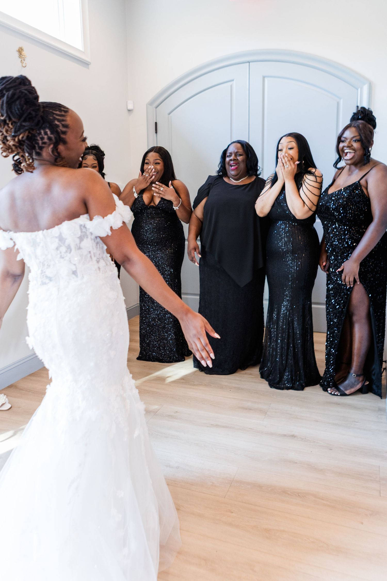 Bridal party wearing sparkly black dresses poses together in bright white room.