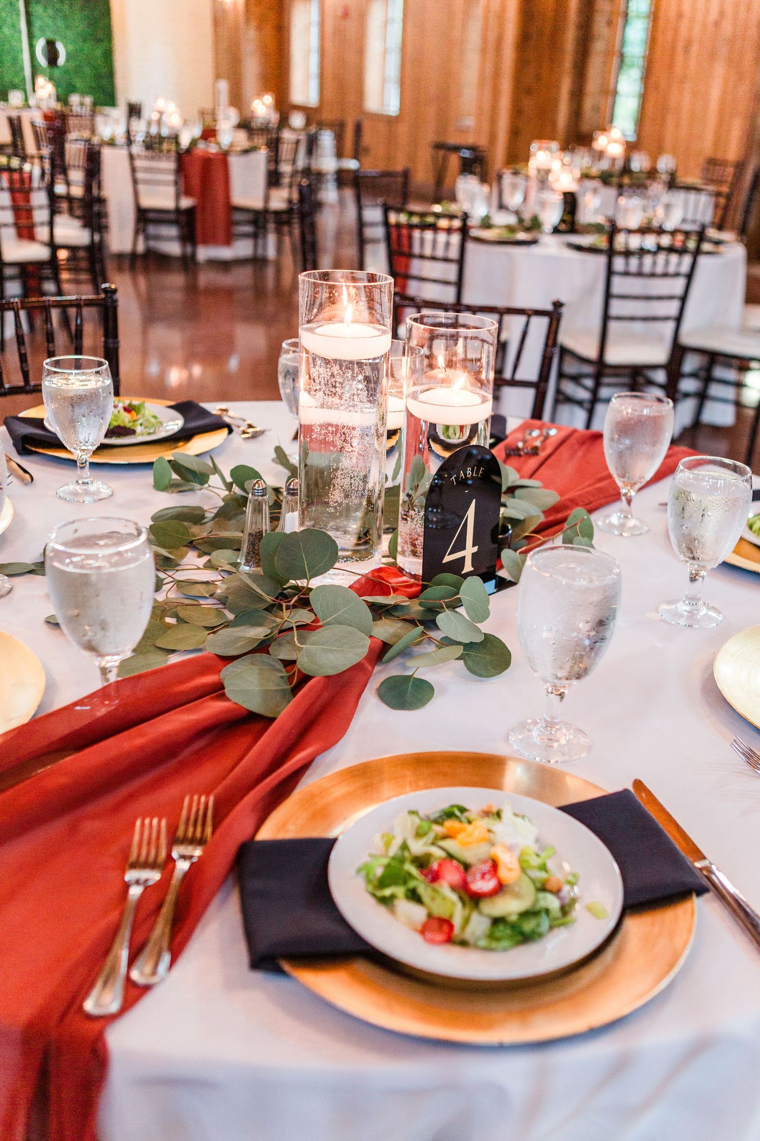 Elegant table settings with red napkins, salad plates and greenery garland at a wedding reception.