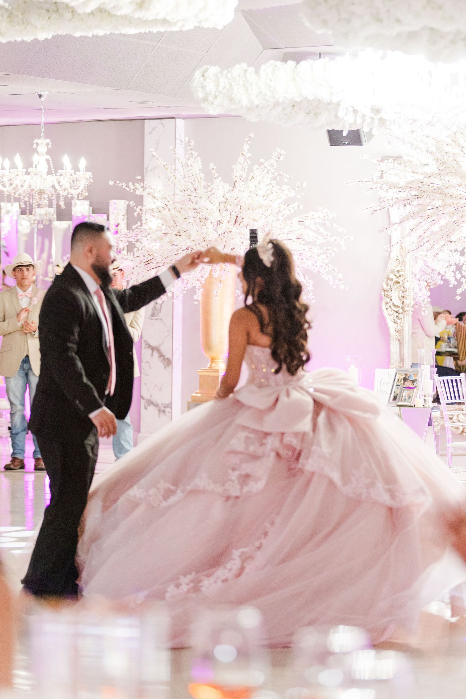 Flowing pink ballgown twirls during a dance in an elegantly decorated white venue.