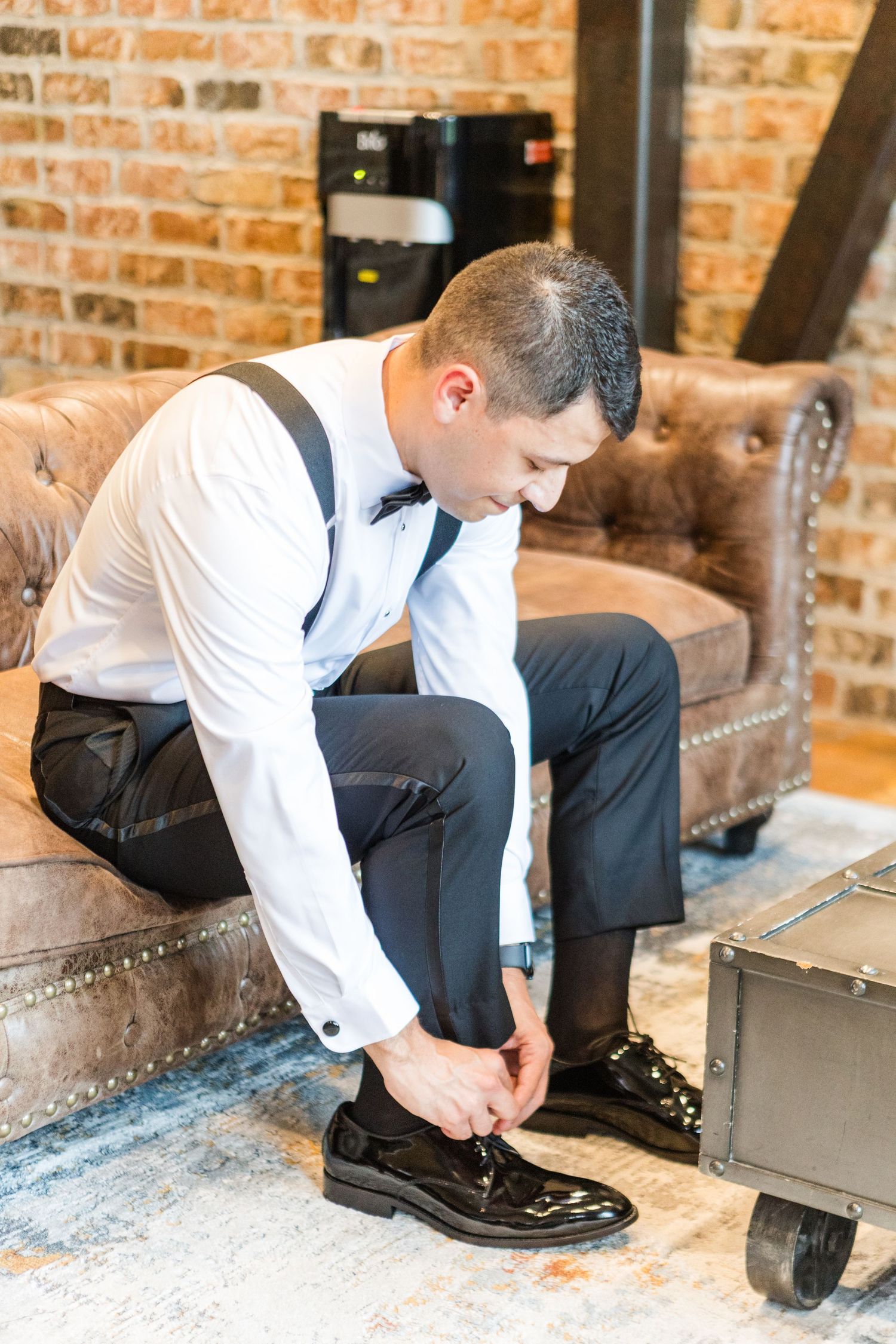 Getting ready scene showing formal footwear preparation against exposed brick wall background.