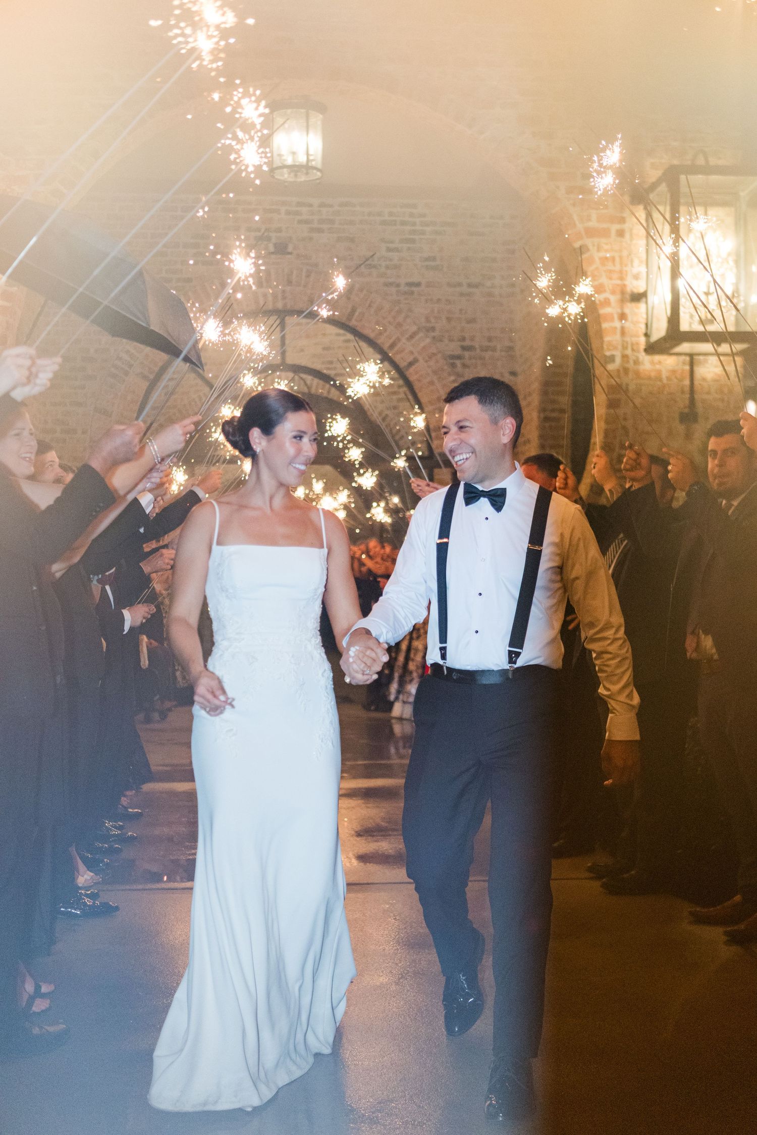 Wedding celebration with a couple walking through glowing sparklers held by guests in an indoor venue.