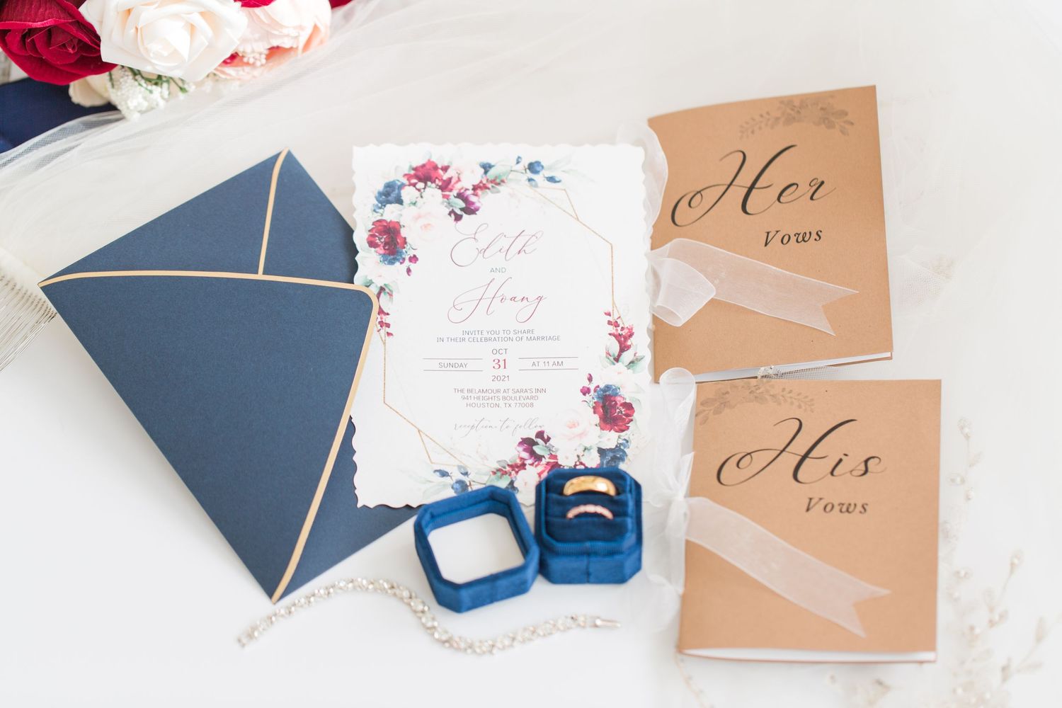 Wedding stationery flat lay with navy blue envelopes, floral invitations and pink roses on white background.